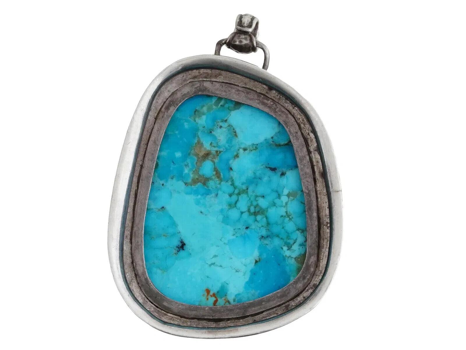 Ein Türkisanhänger in Silber gefasst. Der Anhänger ist mit einem großen, im Cabochon-Schliff geschliffenen Türkis besetzt. Der Türkis hat eine leuchtend blaugrüne Farbe mit einer dunkleren Matrix oder Aderung. Die Lünette hat einen dekorativen Rand