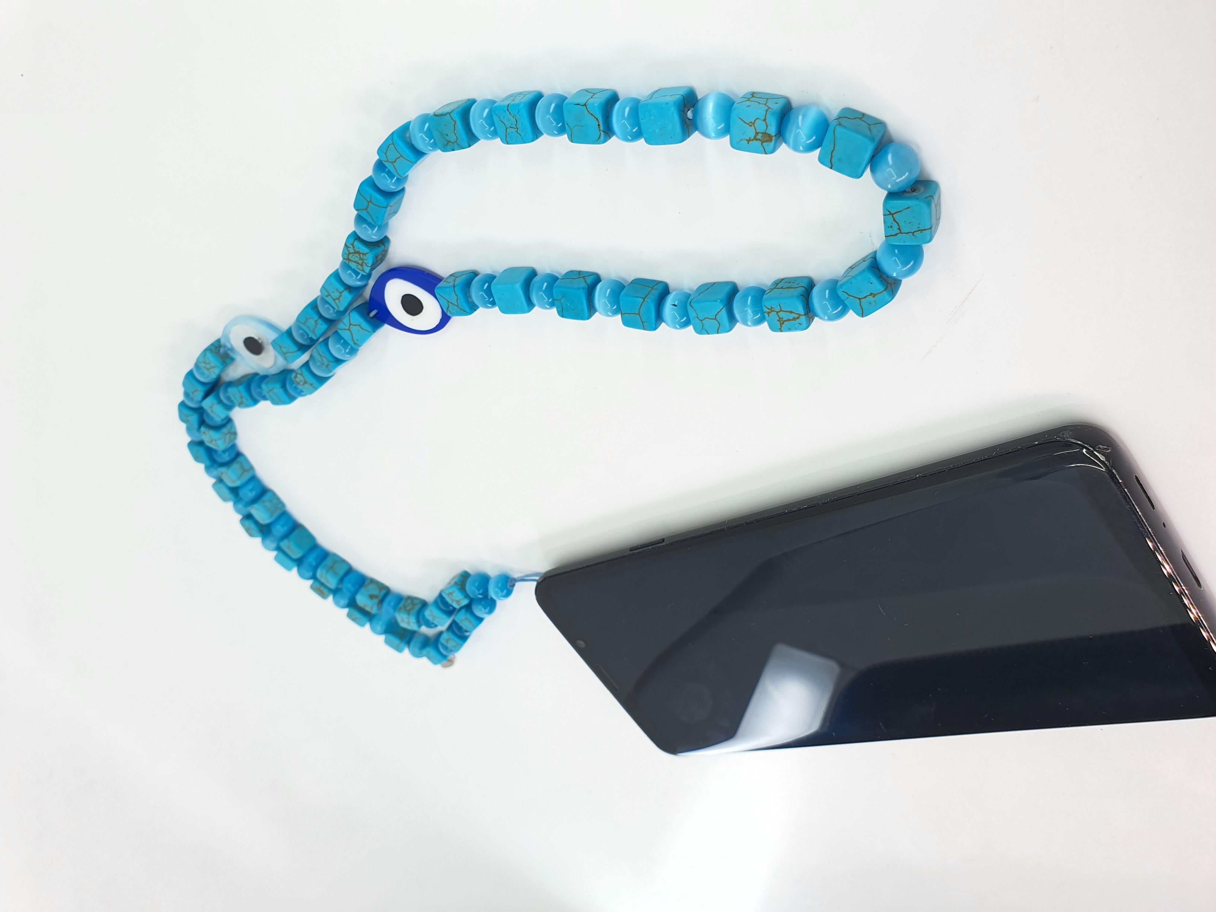 This beautiful combination of turquoise square howlite and blue cat eye beads with 2 charms: dark blue evil eye and light blue evil eye strap can be used as an accessory for a phone, hand bag, like a necklace or body accessory. This fashion strap