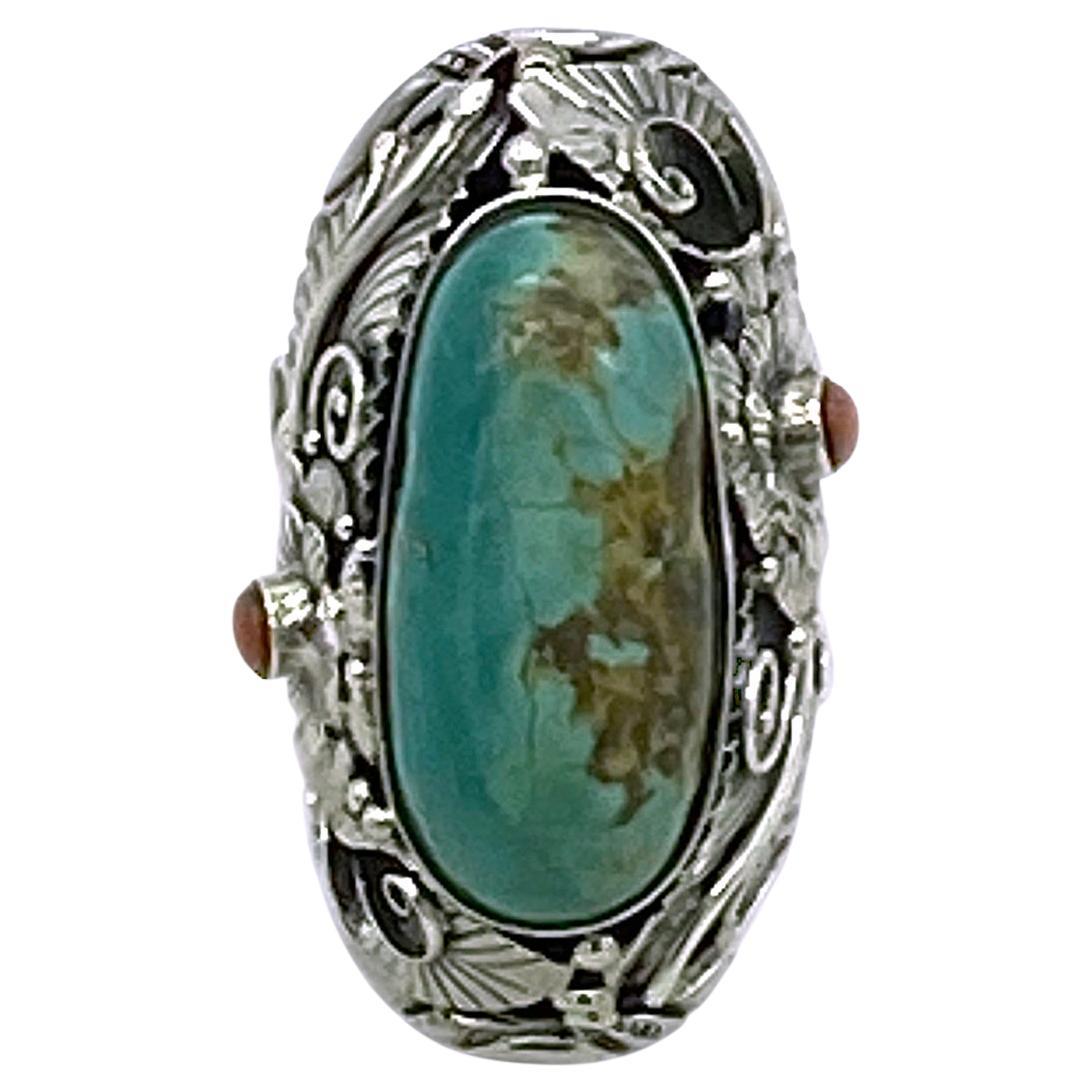 This is a large turquoise sterling cocktail ring.  It has a 31 mm x 15 mm polished turquoise cabochon and two 4mm corals bezal set in a sterling silver adjustable unisex ring with a richly detailed flower and leaves pattern.

Our vintage jewelry