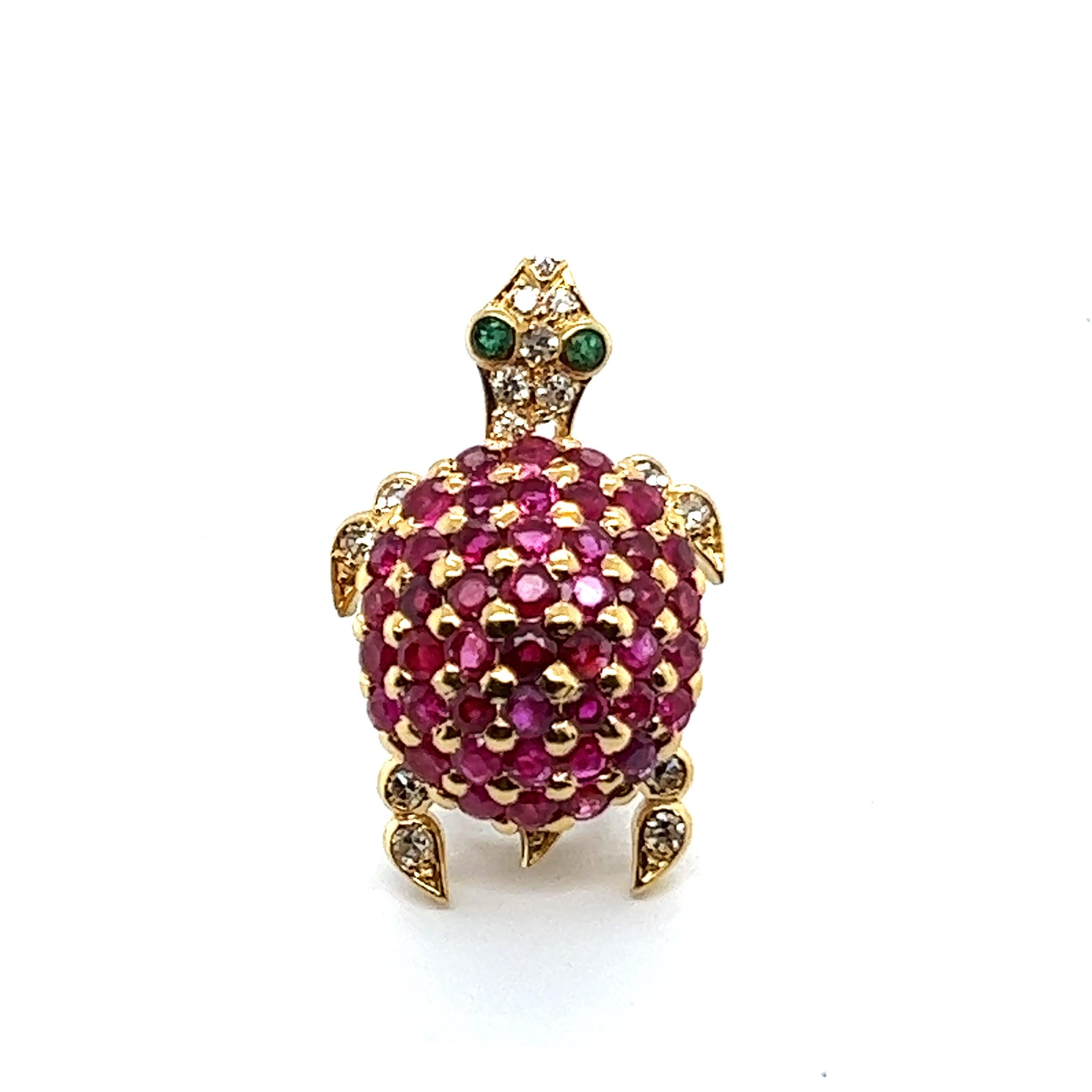 Presenting a playful turtle brooch with rubies and diamonds in 18 Karat yellow gold.  A little baby turtle features a lustrous body adorned with 44 round rubies, totaling 1.34 carats, while its eyes sparkle with two round emeralds. The delicate legs
