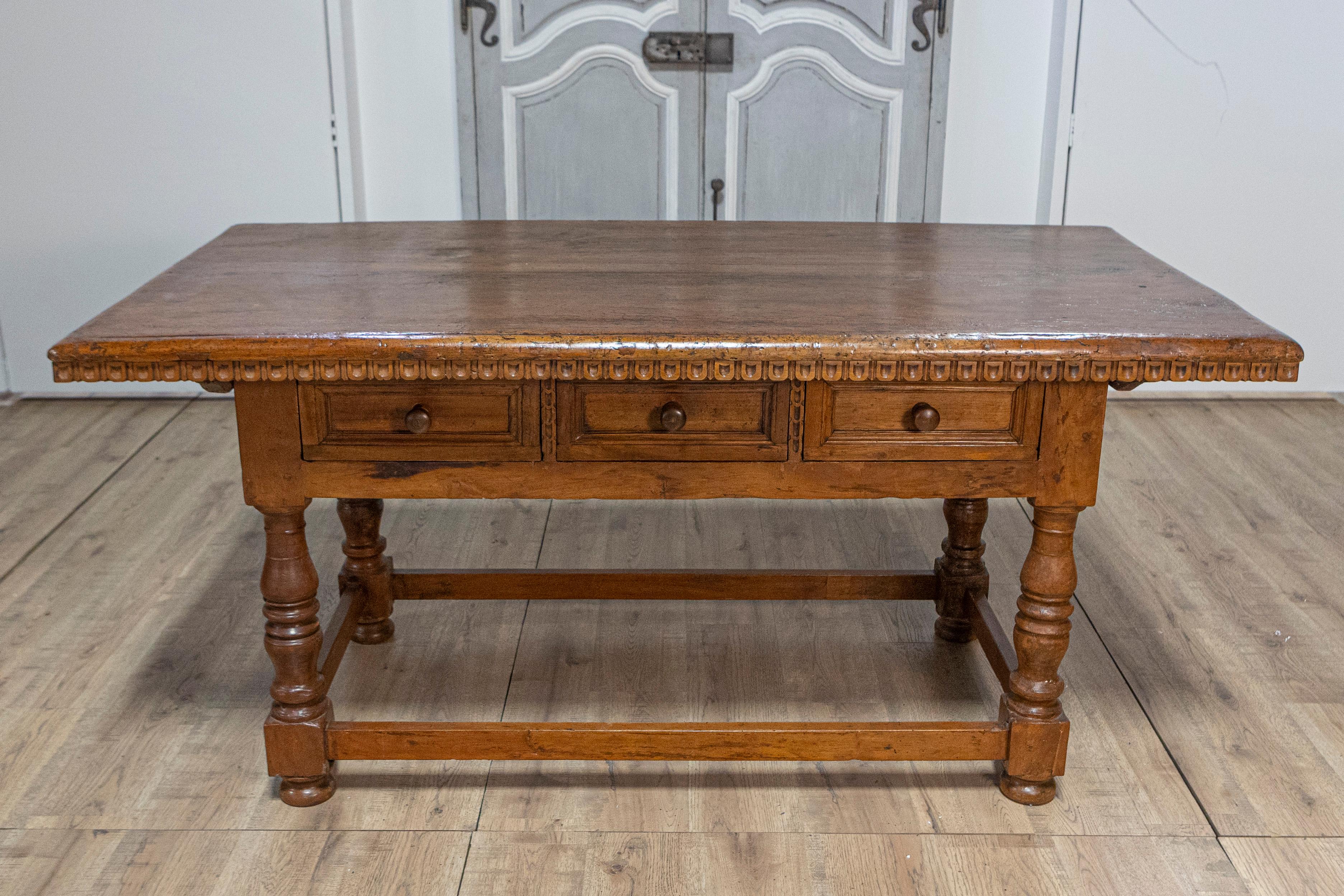 An Italian Tuscan walnut refectory table from circa 1790 with carved scoop motifs, three drawers, turned legs and plain side stretchers. This Italian Tuscan walnut refectory table from circa 1790 embodies the charm and craftsmanship of 18th-century