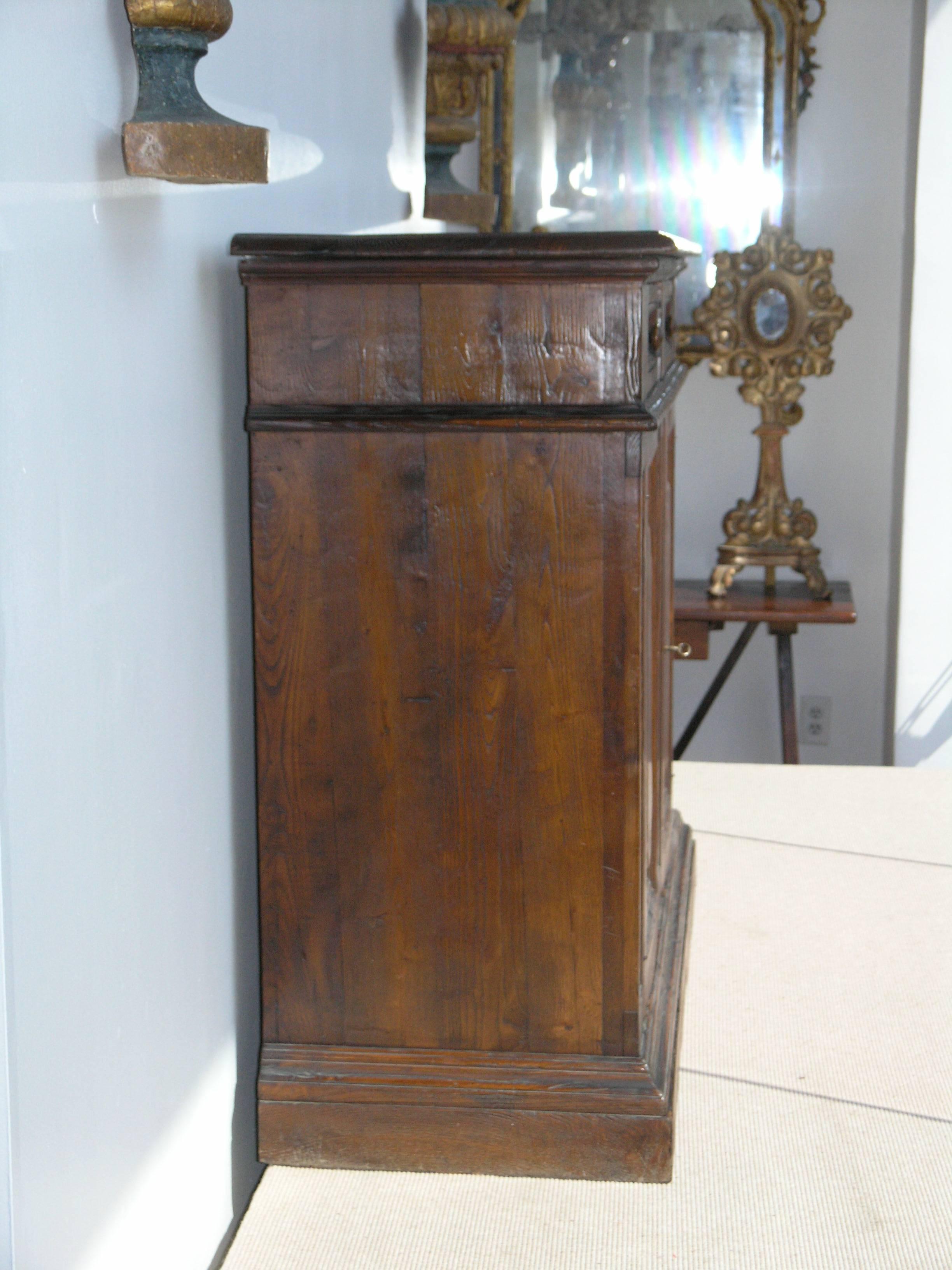 Rectangular top with molded edge over two drawers above two paneled doors raised on plinth base.