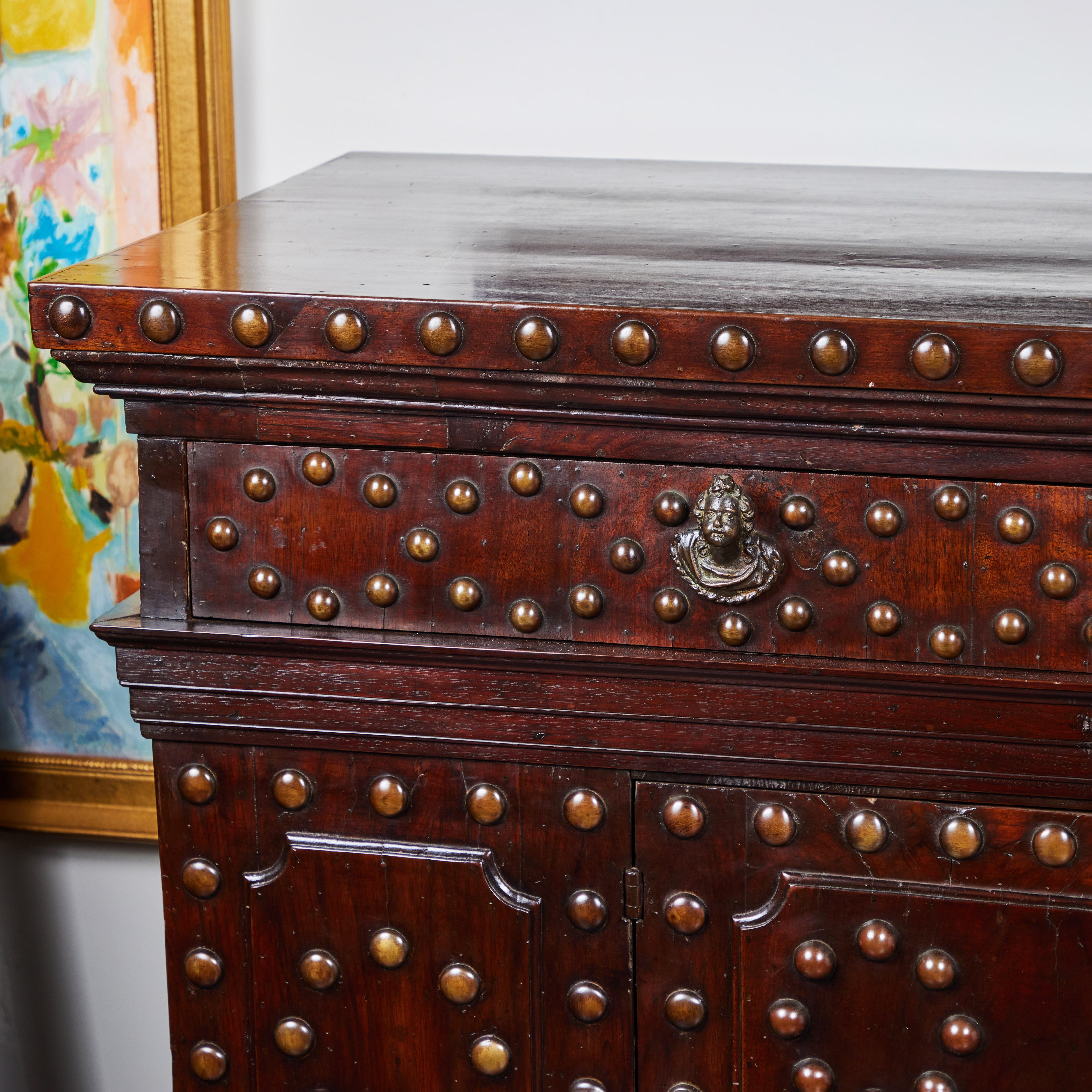 A handsome Tuscan walnut buffet with patinated bronze studs on the front with bronze cherub head knobs and raised panels on sides. One drawer, 2 doors. One interior shelf.