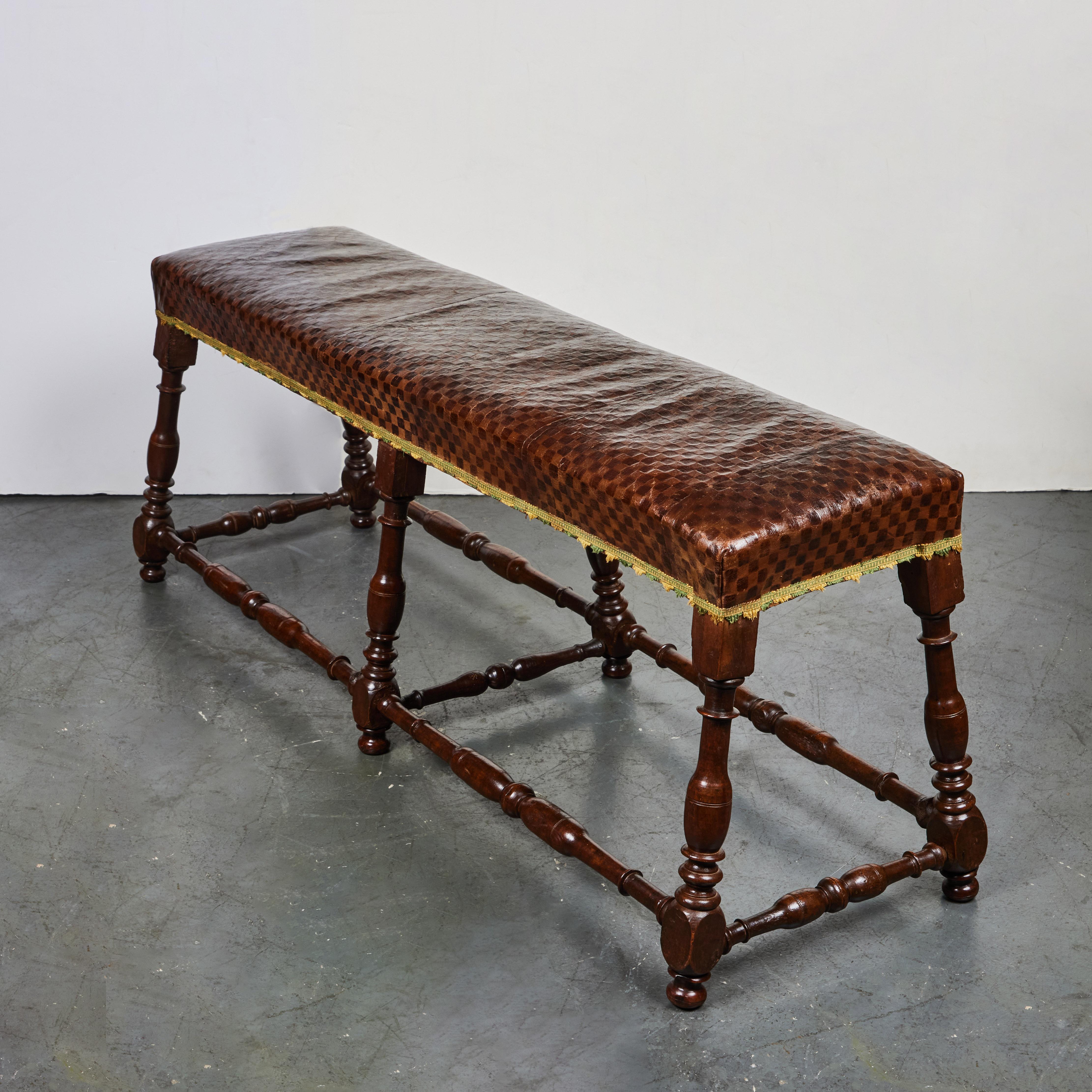 A hand carved walnut bench with 2 stretchers, checkered patterned leather and finished with woven trim.  From the area of Tuscany.
