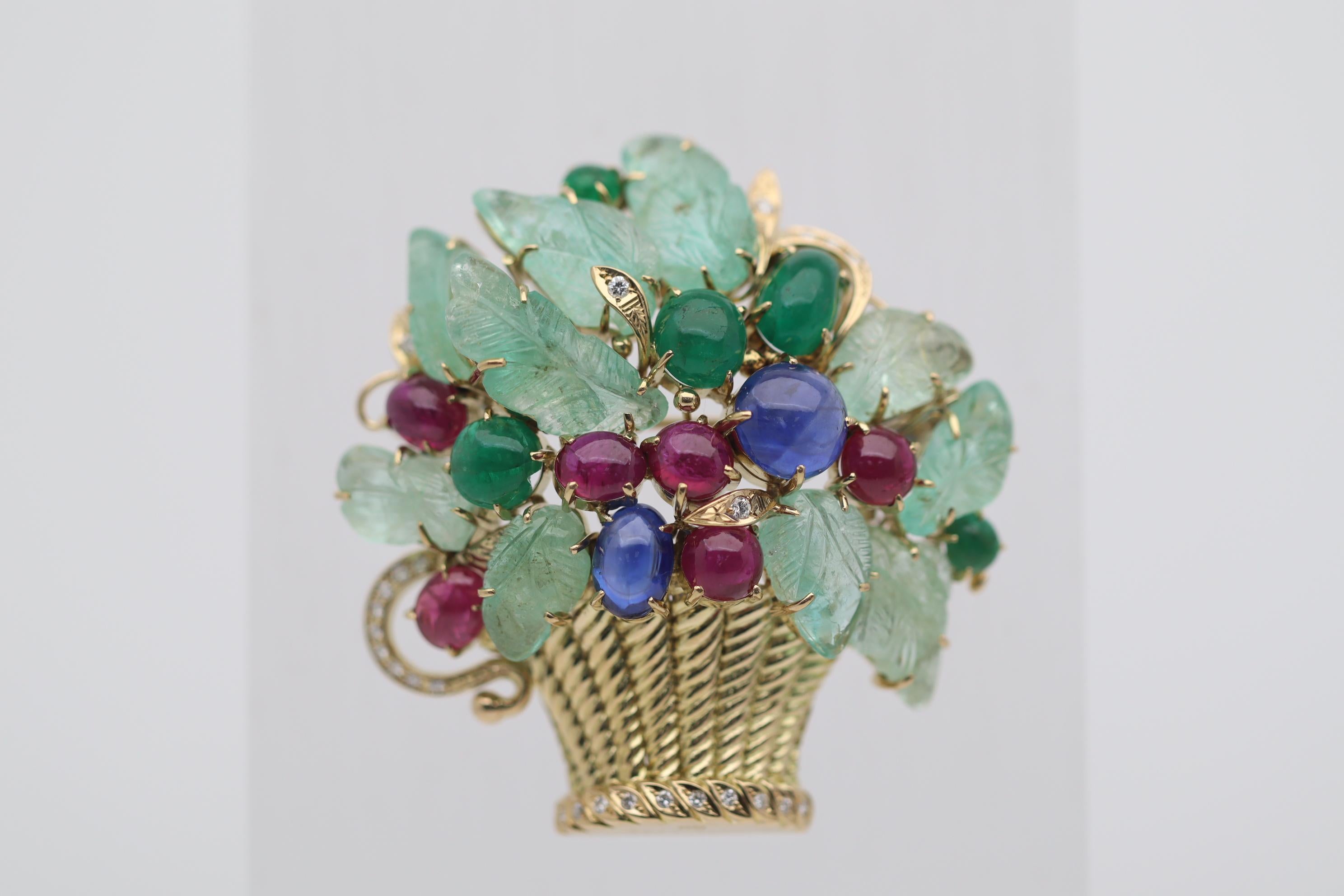 A fantastical deco-style Tutti Frutti brooch featuring large carved and cabochon emeralds along with cabochon rubies, sapphires, each having rich intense color which contrast and complement each other. There are 0.27 carats of round brilliant-cut