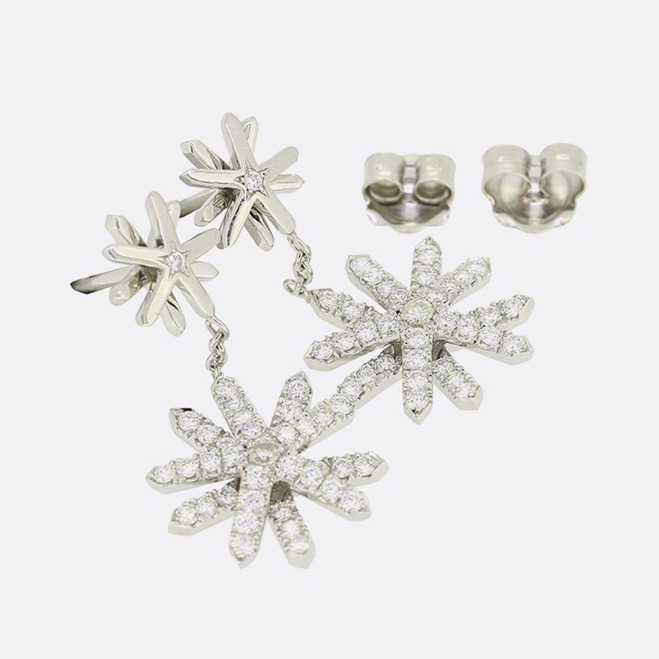 This is a beautiful pair of diamond drop earrings. Each earring features a plain snowflake which has been star set with a single round brilliant cut diamond. Additionally, the earrings have a suspended diamond snowflake which hangs freely by chain.