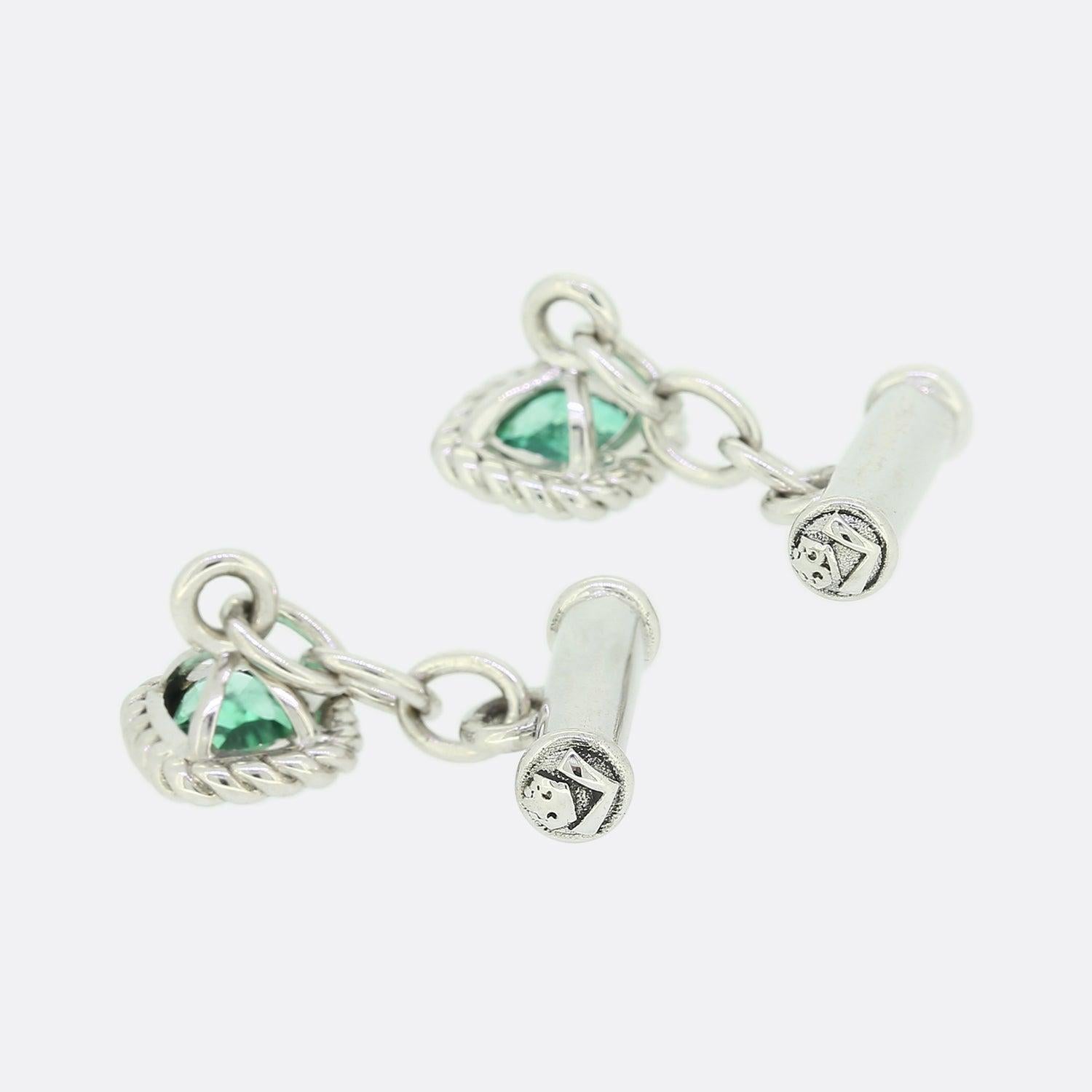 Si tratta di un paio di gemelli in oro bianco 18ct di eccezionale fattura. Ogni gemello ospita uno smeraldo naturale a cuscino in un'incastonatura a sfregamento e una catena che conduce al retro della barra. La barra è stata intagliata con il logo