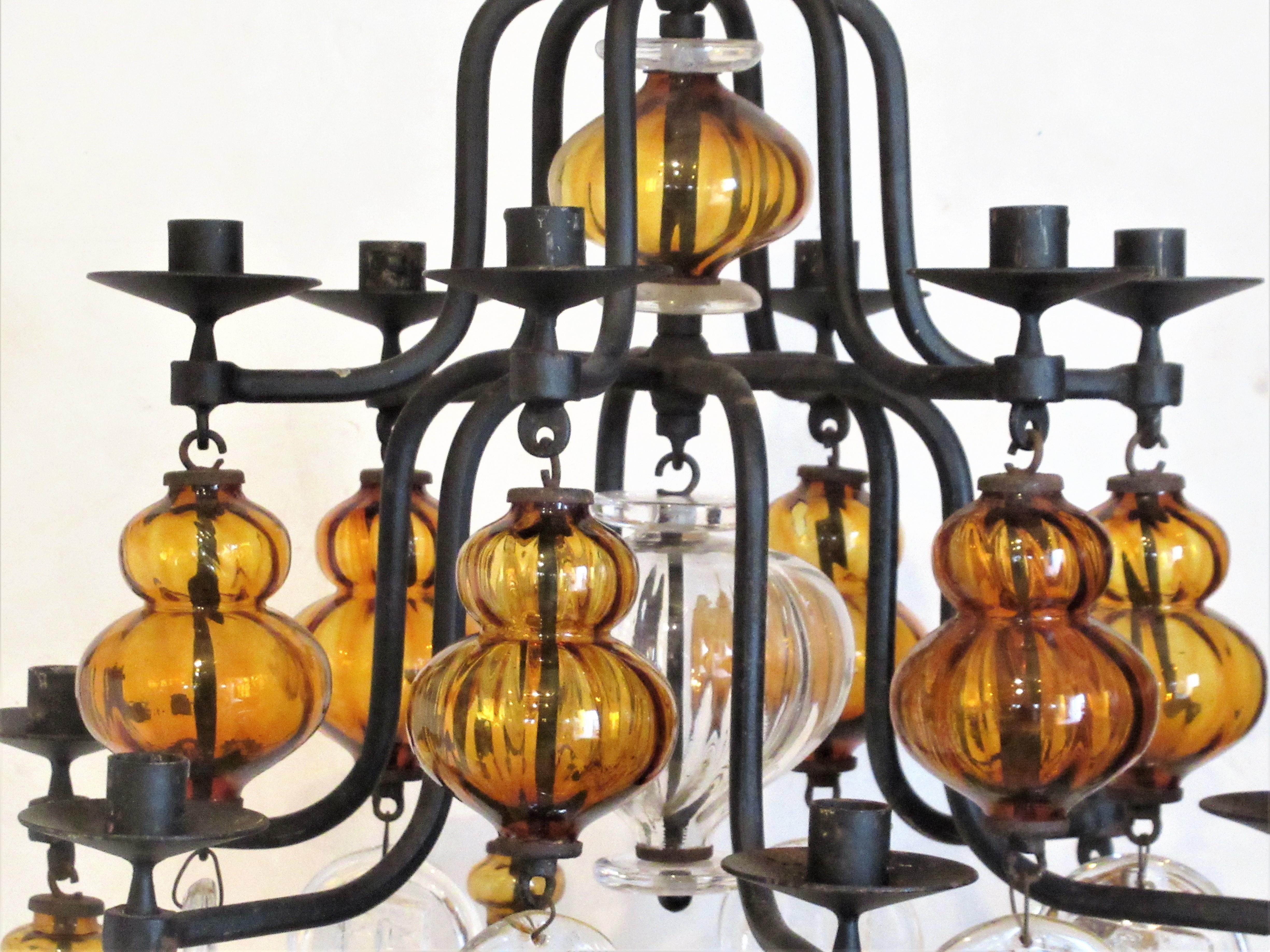 Large hand wrought iron twelve candle armature chandelier with both amber / clear glass elements and solid clear glass pendants showing images of fish and faces by Erik Hoglund for Boda Glassworks, Sweden - circa 1950's. Chandelier measures 36