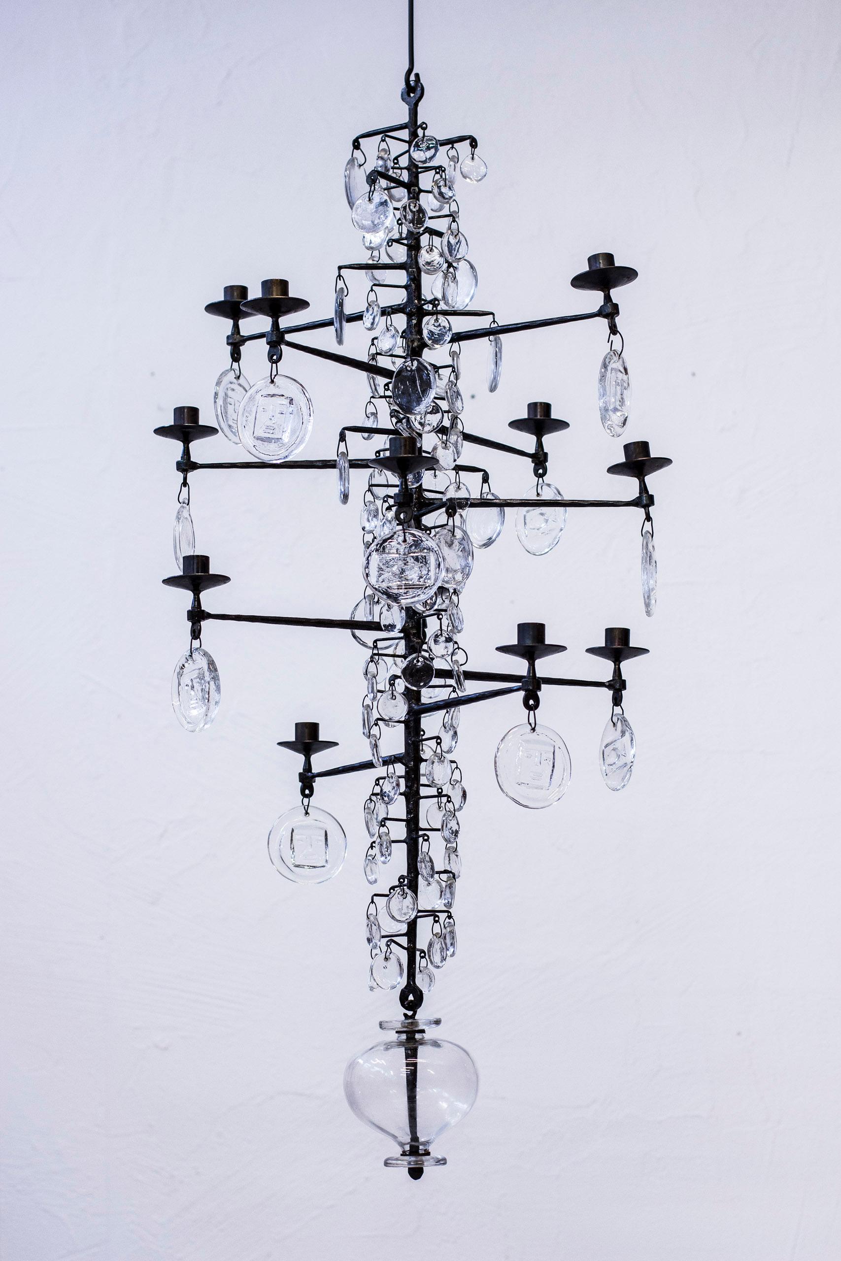 Large twelve-armed chandelier designed by Erik Höglund. Produced in Sweden by Boda Smide. Made from wrought iron and handblown clear glass with Höglund signature motifs of faces and figures. Excellent original condition with light age related