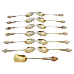 Twelve gilded silver teaspoons and sugar shovel with applied relief handles