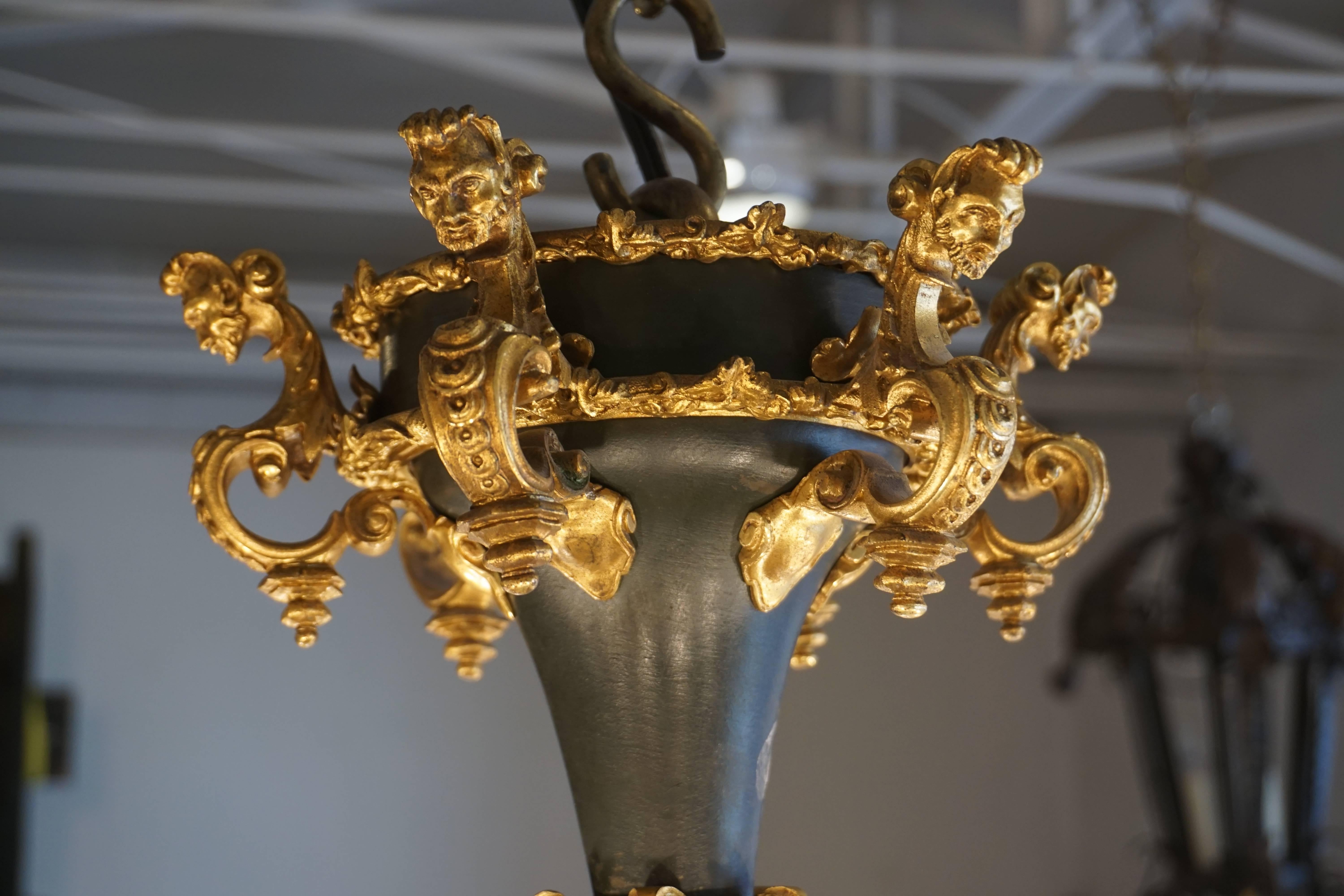 Der zwölfflammige Barockkronleuchter ist in Bronze, vergoldet und dunkelbronzefarben gehalten und mit süßen Puttengesichtern versehen. Es ist eine hübsche Leuchte mit viel Charakter, komplizierten Schnitzereien und reich an Farben. Eine wunderbare
