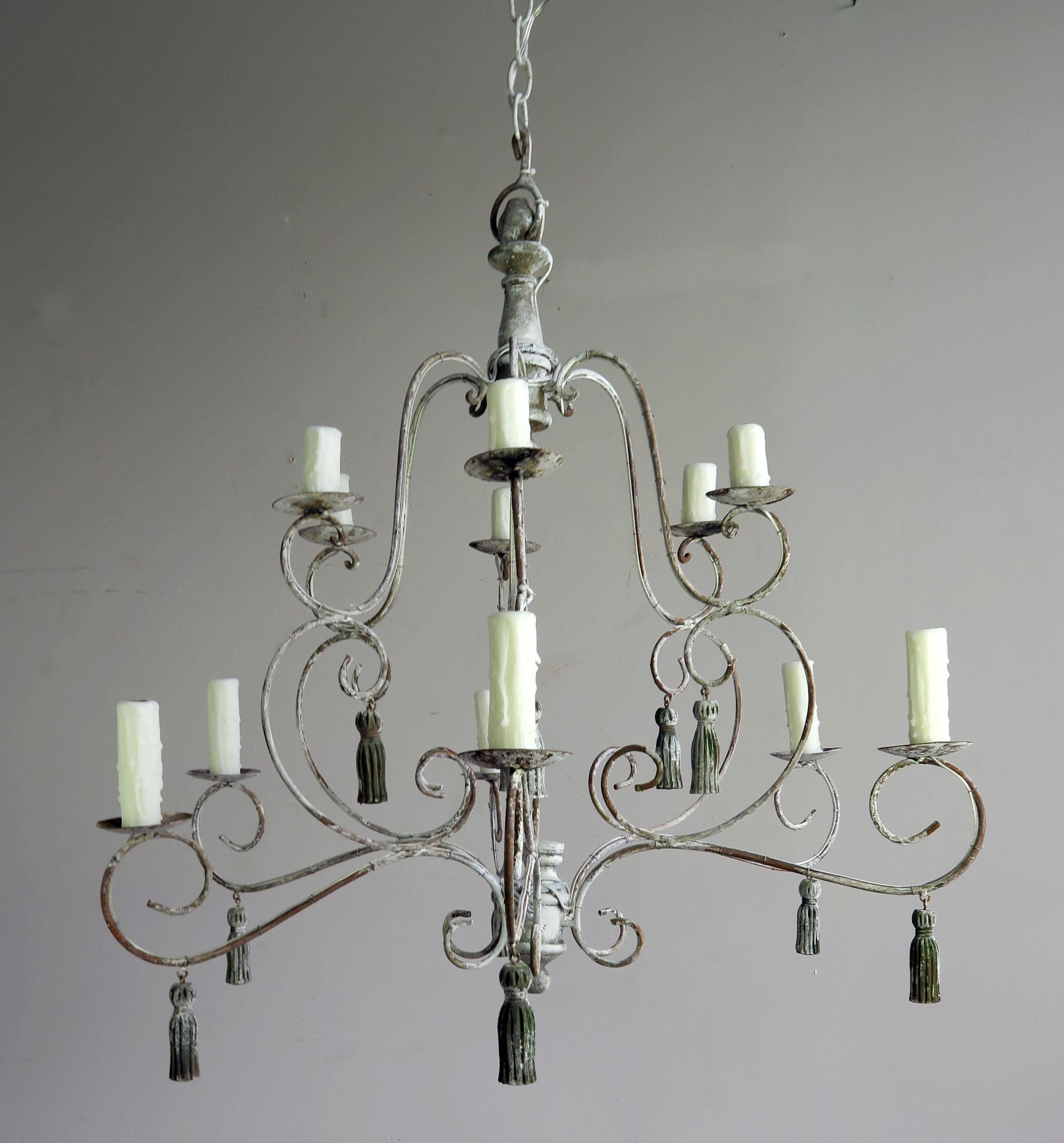 Twelve-light French iron and wood chandelier with beautiful worn painted finish. The fixture is newly rewired with drip wax candle covers. The chandelier includes chain and canopy. Twelve carved wood painted tassels throughout.