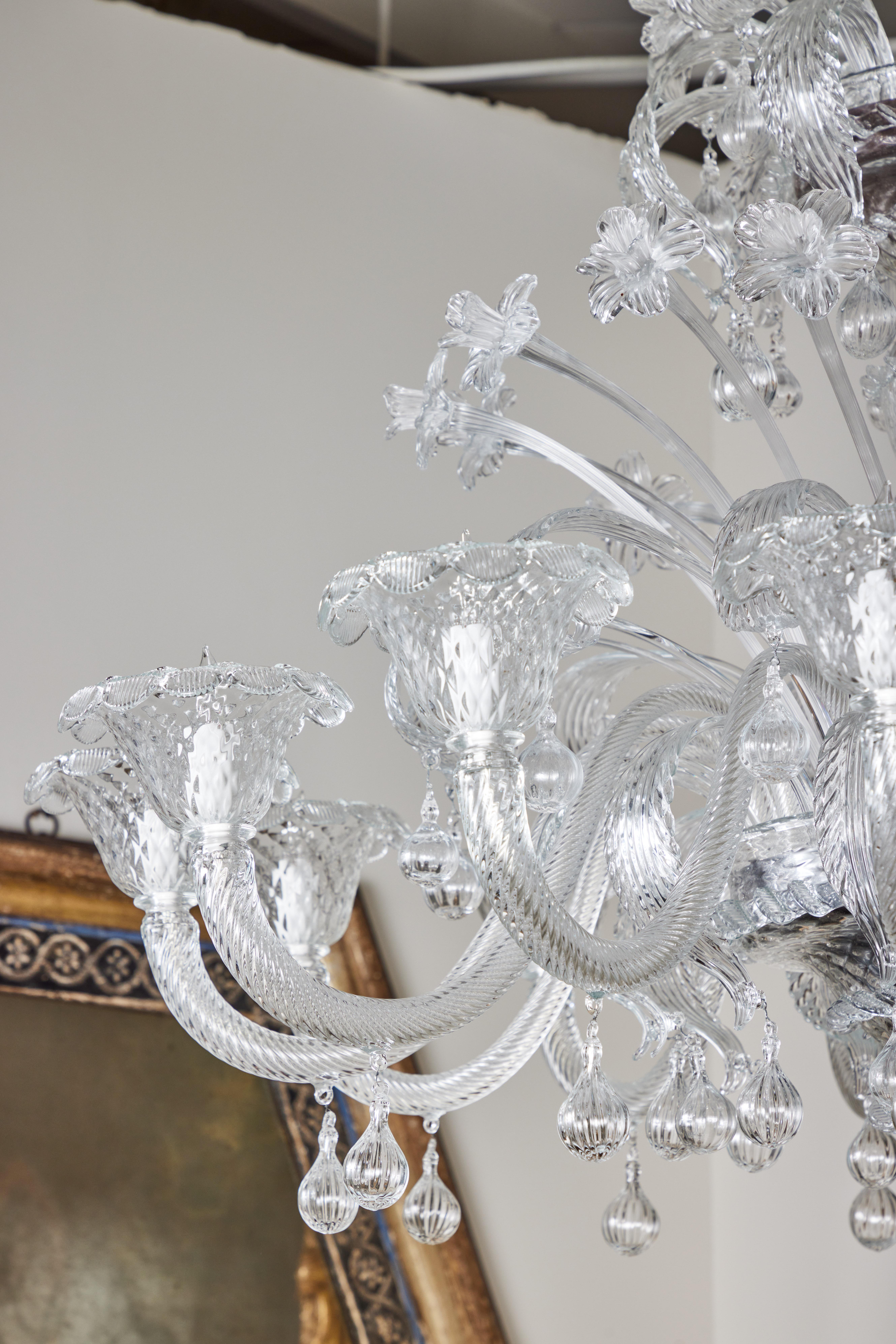 Ein vierstöckiger italienischer Muranokronleuchter mit Silberverzierung und zwölf Lichtern. Die oberen Ebenen sind mit trompetenförmigen Blüten und kaskadenförmigen Blättern verziert. Die zwölf Reticello-Arme erheben sich zu floralen Bechern und