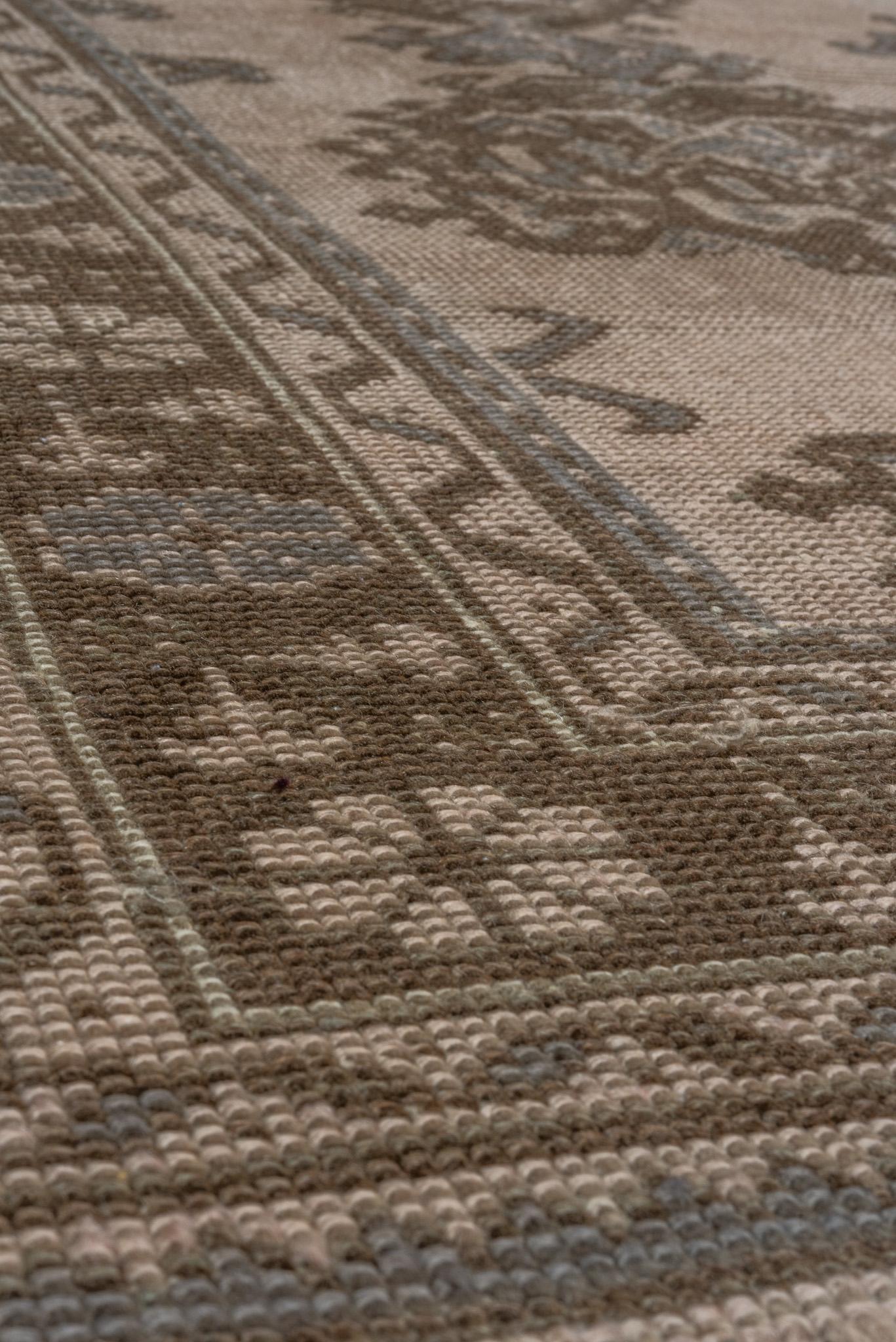Dieser atemberaubende Oushak-Teppich mit den Maßen 7,1 x 10,0 Fuß verkörpert die zeitlose Schönheit der türkischen Handwerkskunst. In einer sanften, erdigen Farbpalette aus gedämpften Taupetönen und Brauntönen zeigt das zentrale Feld des Teppichs