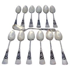 Twelve silver coffee spoons and sugar shovel with patinated relief handles