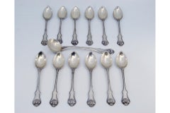 Twelve silver teaspoons and sugar scoop with appliqués and shell handles