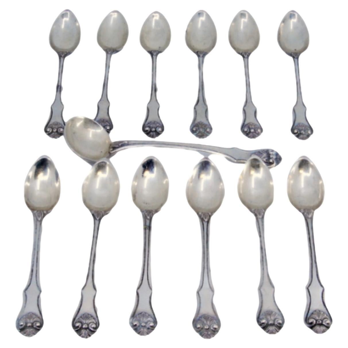 Twelve silver teaspoons and sugar scoop with appliqués and shell handles