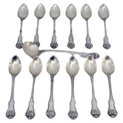 Twelve silver teaspoons and sugar scoop with appliqués and shell handles