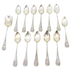 Twelve silver teaspoons and sugar shovel with floral relief monograms