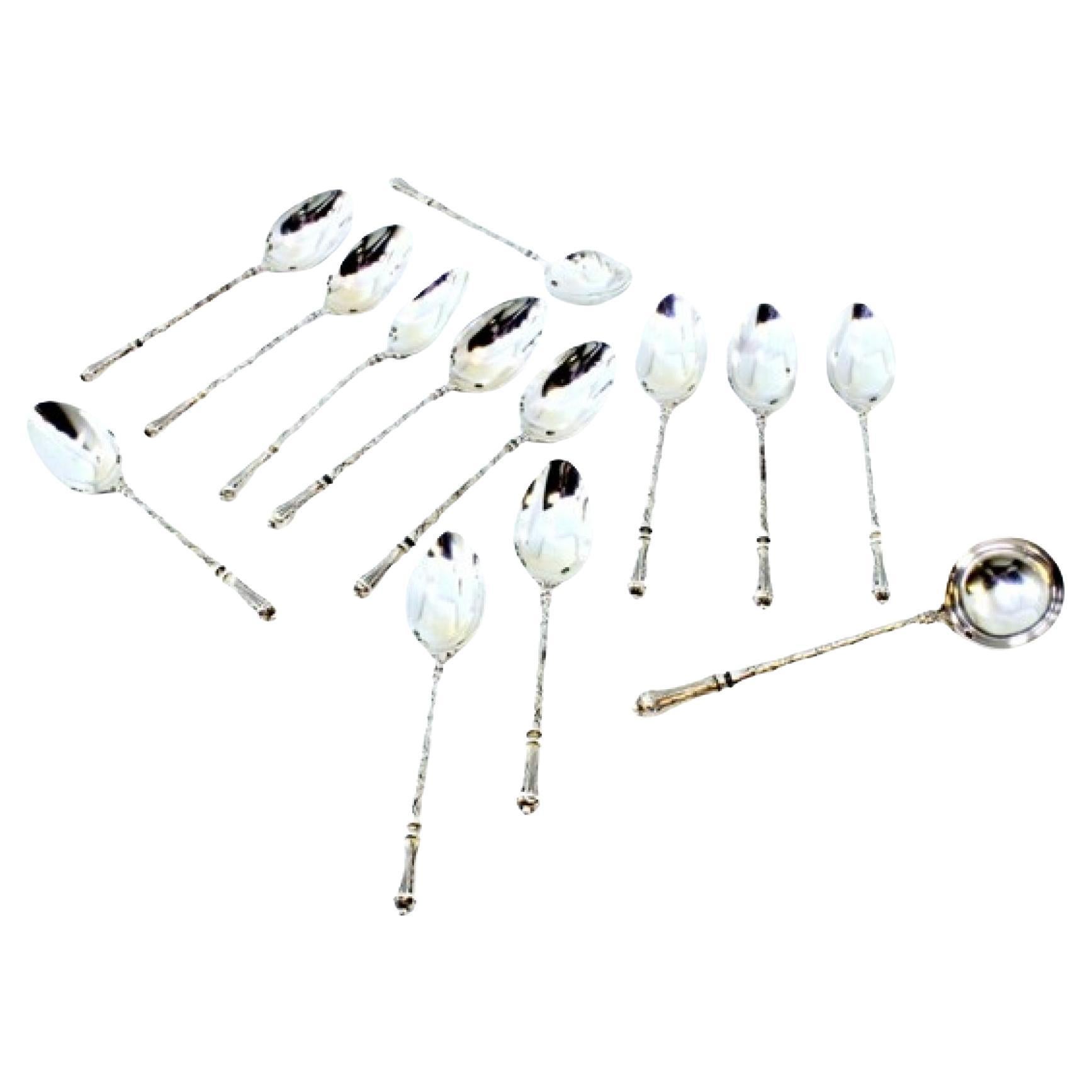 Twelve silver teaspoons and sugar shovel with friezed relief handles