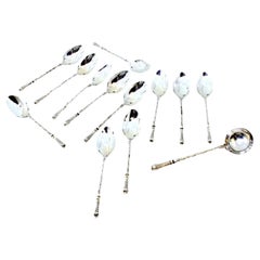 Twelve silver teaspoons and sugar shovel with friezed relief handles