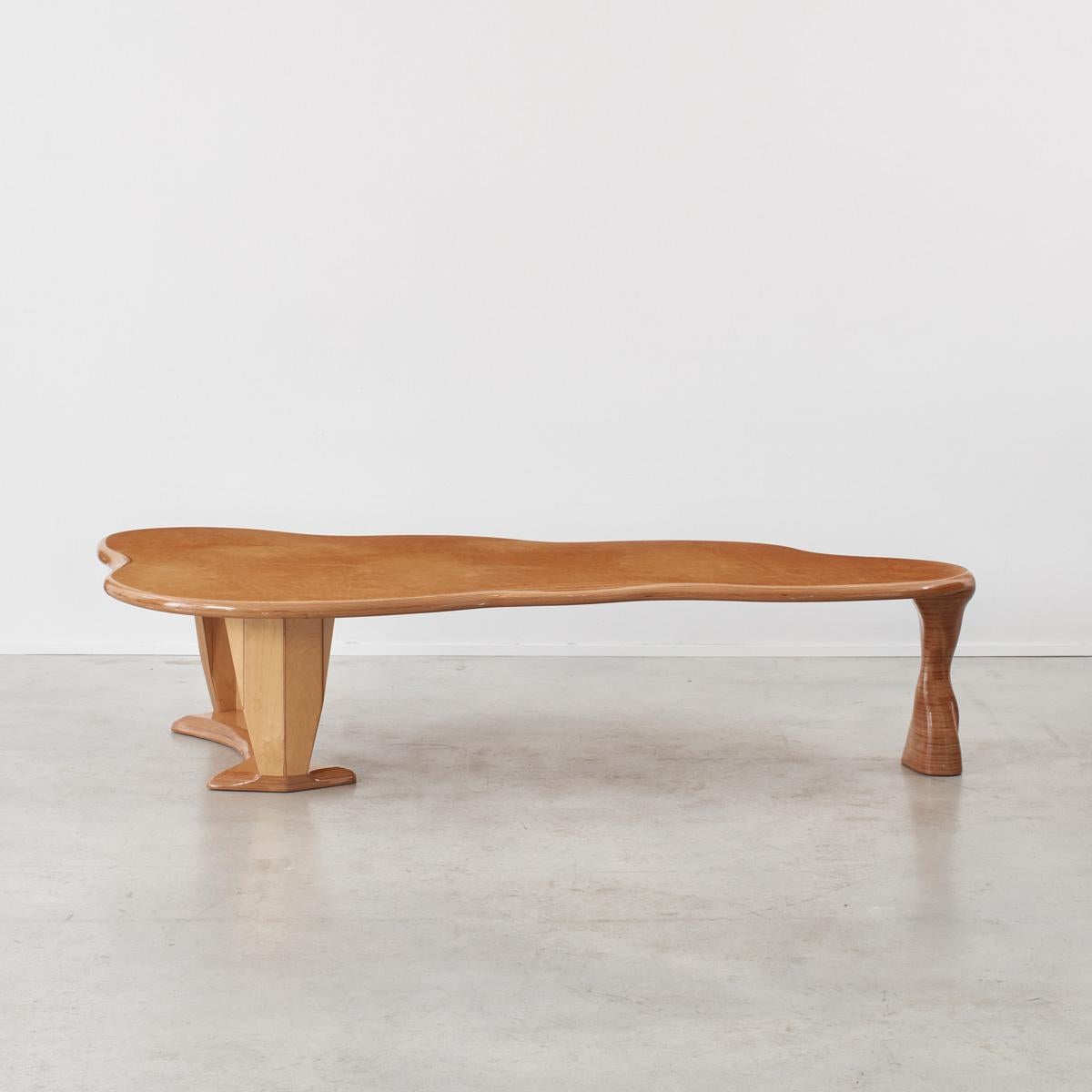 A beautifully constructed, organic-formed table on three legs. The single leg has been sculpted into the form reminiscent of an animal’s leg, and the rear legs, set upon a base, possess a more machined aesthetic.