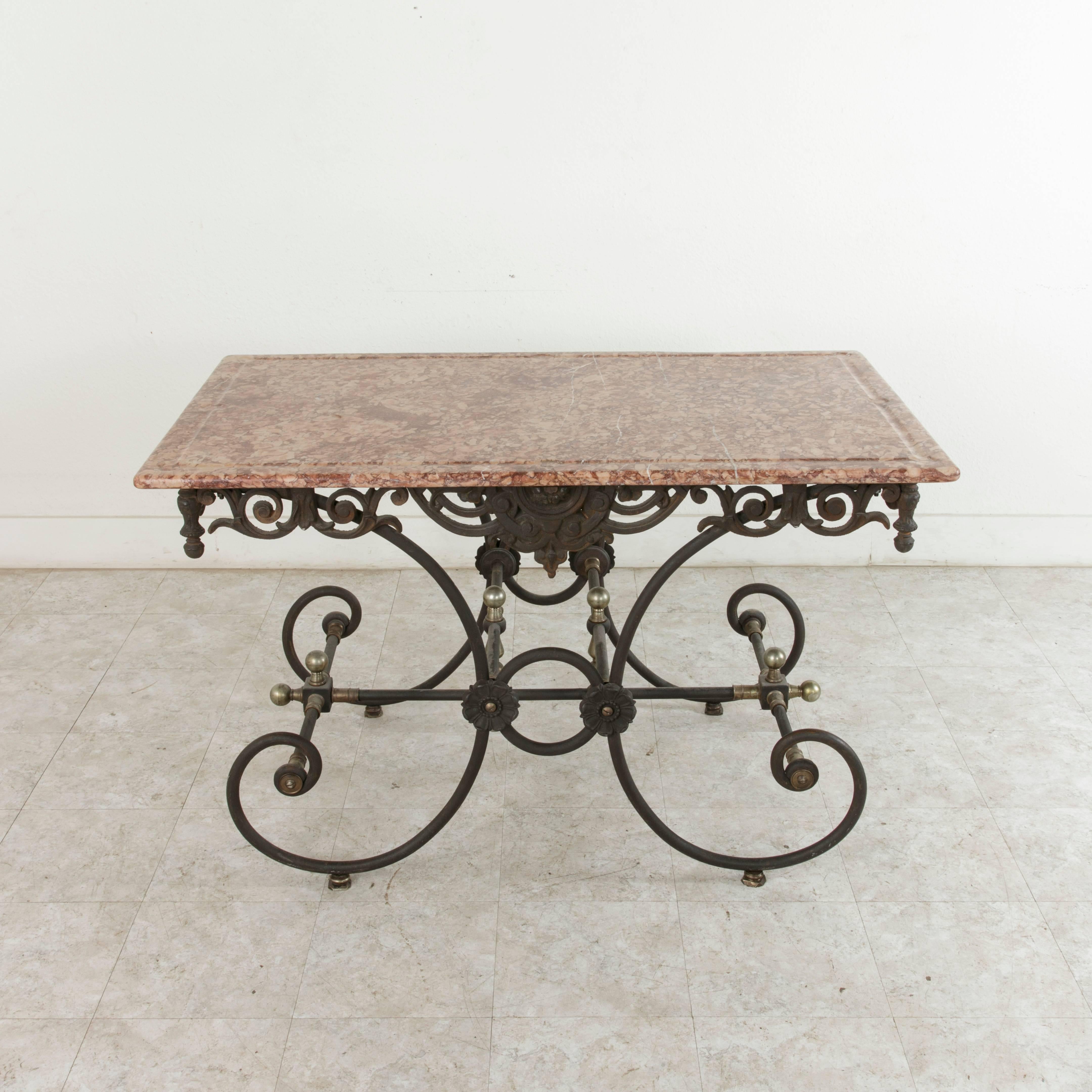 This 20th century French iron pastry table or butcher's table features a solid rose-colored marble top with a groove around the perimeter which was intended to catch blood when the butcher was at work. An intricately scrolled apron supports the