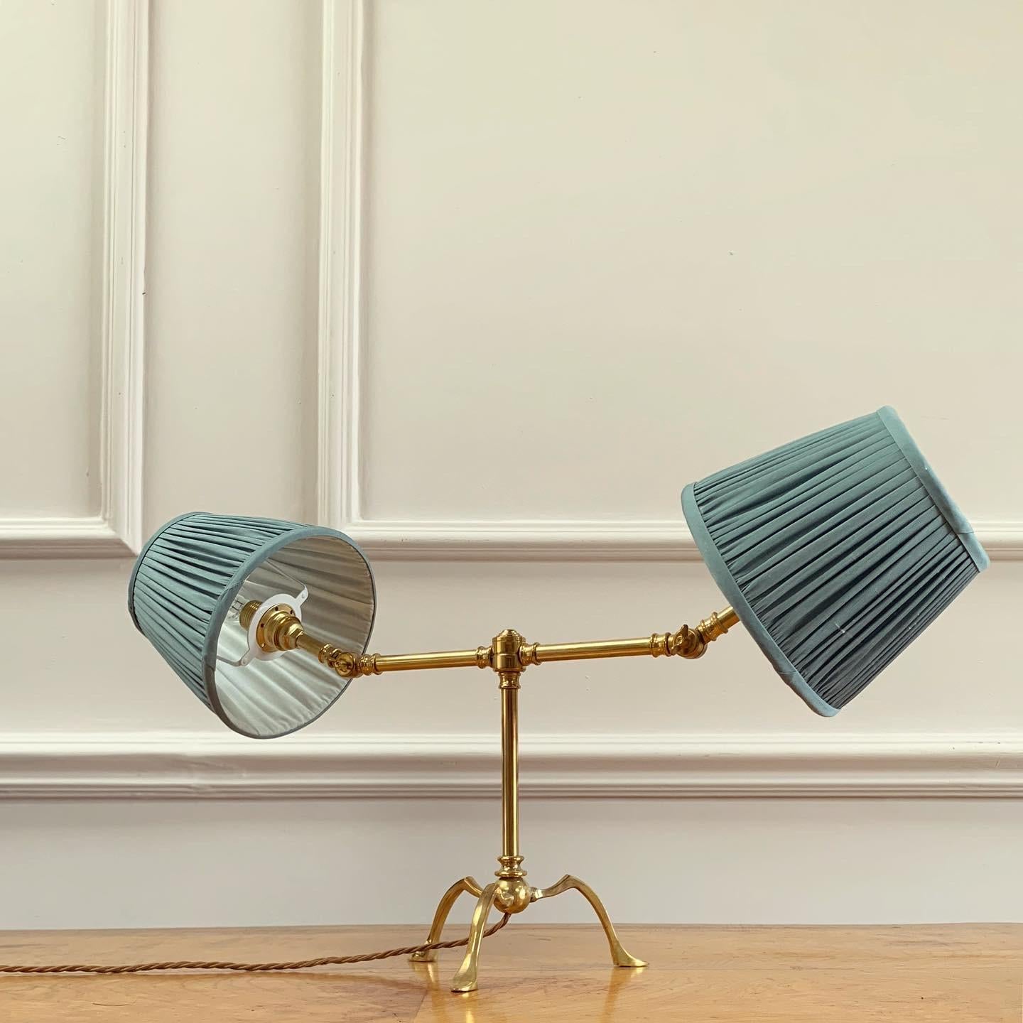 A brass table or reading lamp with adjustable twin arm bulb holders and stem supported on a tripod base - this design inspired by the arts and crafts legendary designer W.A.S Benson.

Shown with antique linen pleated lampshades - available