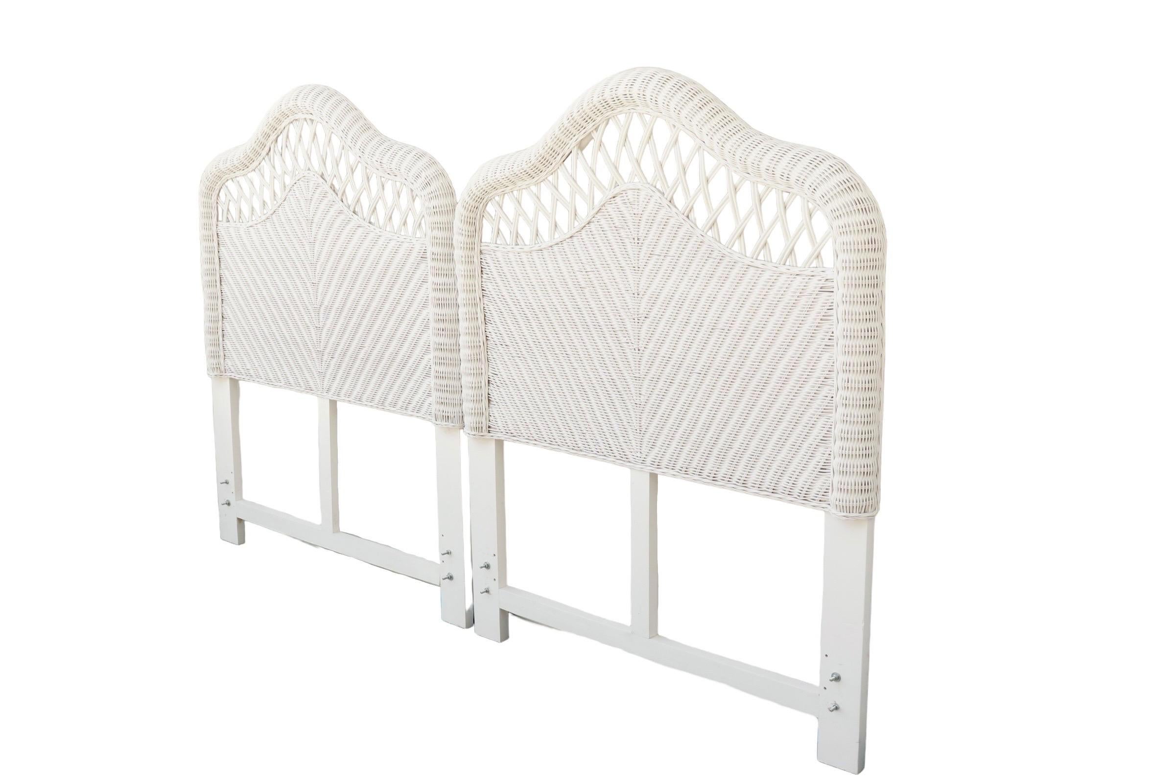 A pair of white Heywood Wakefield style twin size wicker headboards. Bentwood bamboo and wooden frames support curved woven rattan in a camel back shape. Decorated with an open weave panel above a chevron woven back. Finished with a twist braid trim