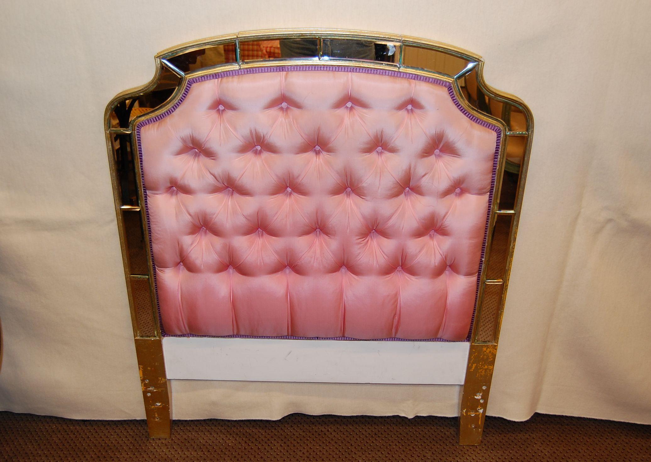 Twin size headboard with tufted silk upholstery and a mirrored edge around the perimeter. The top of the headboard has a panel that folds forward, which originally concealed a bed lamp. Overall good condition, mirror has some age related defects,