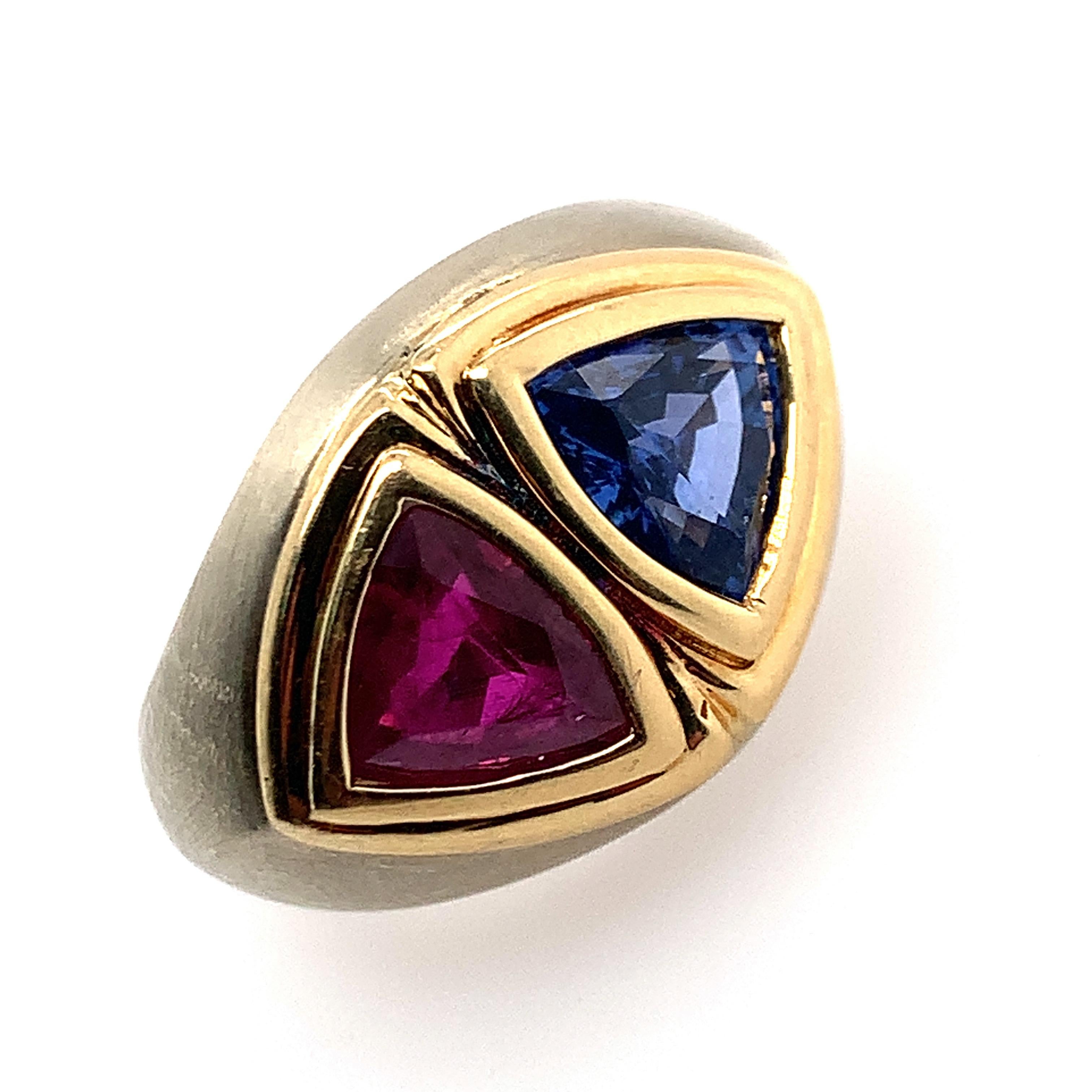 The broad tapering band of bezel-set Toi et Moi design, set with a trilliant-cut sapphire weighing approximately 1.45 carats and a ruby weighing approximately 1.40 carats, in brushed textured and polished 18k white and yellow gold, size 5