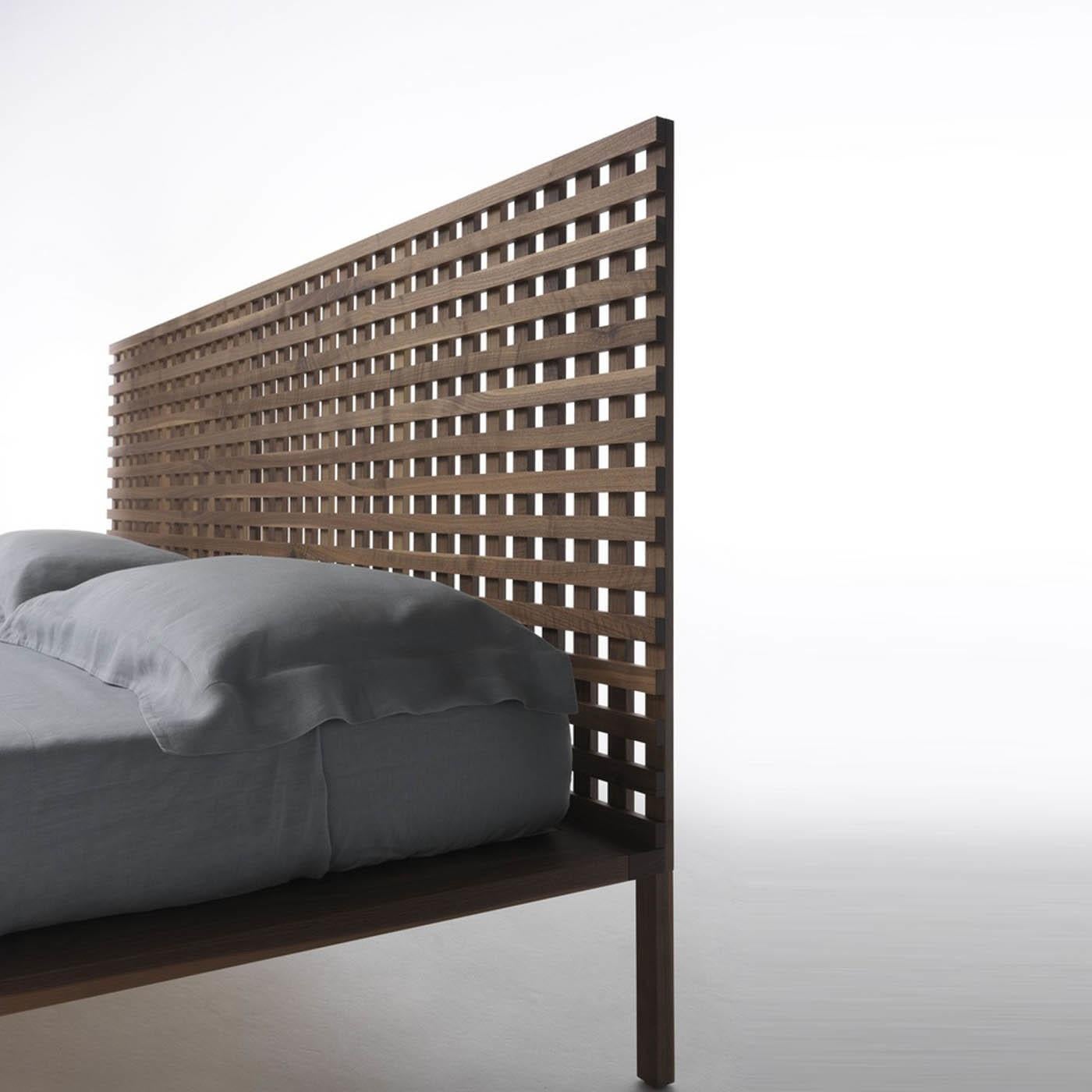 Completely made of solid Canaletto walnut, this striking bed by Matteo Thun and Antonio Rodriguez boasts a unique and captivating design. It features a headboard made of orthogonal slats giving shape to a fine and distinctive fretwork. An example of