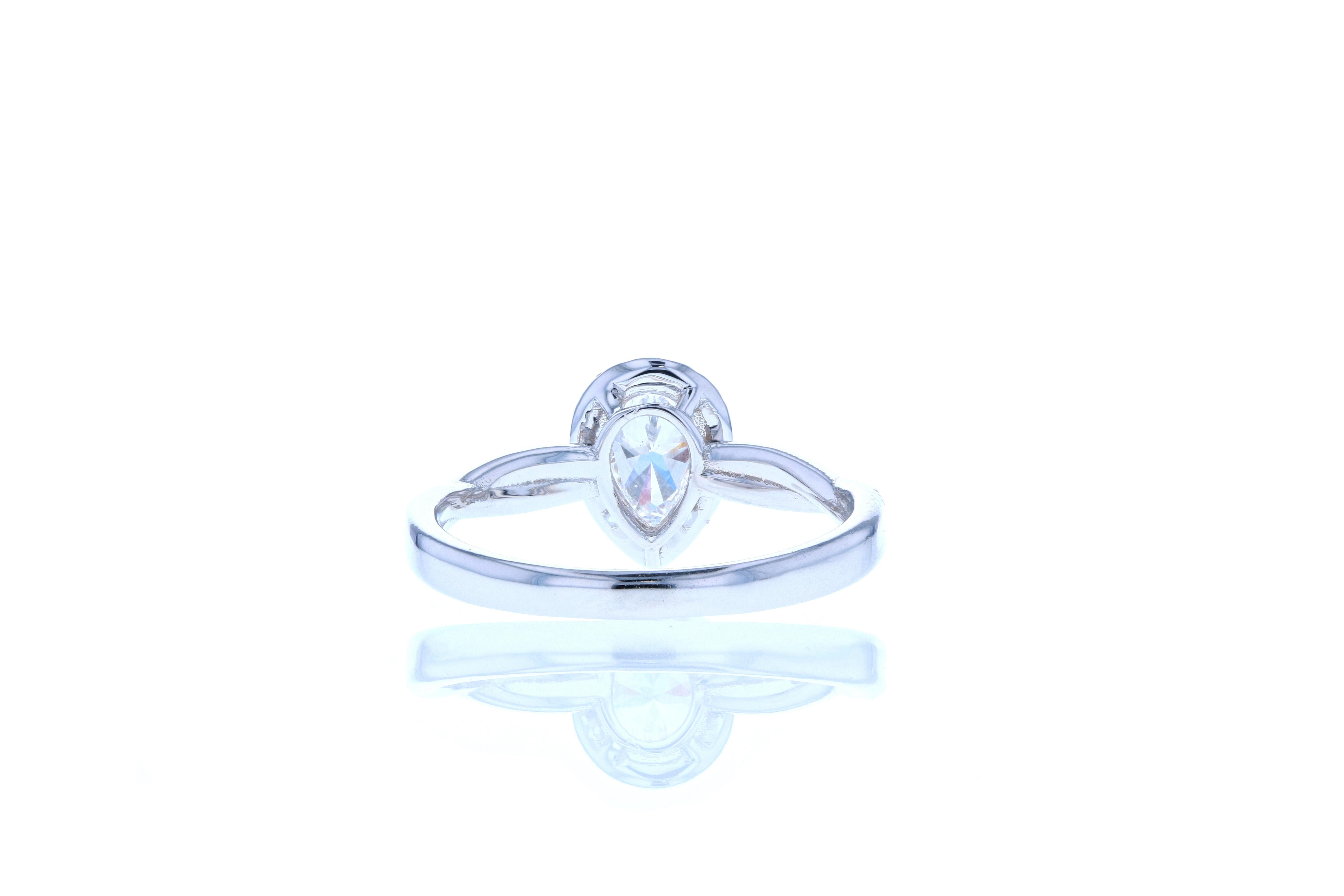 A dainty and elegant pear shaped diamond engagement ring featuring pear shaped center diamond surrounded by a delicate diamond halo to increase the perceived size of the center stone. The shank is an elegantly undulating band with one row of diamond