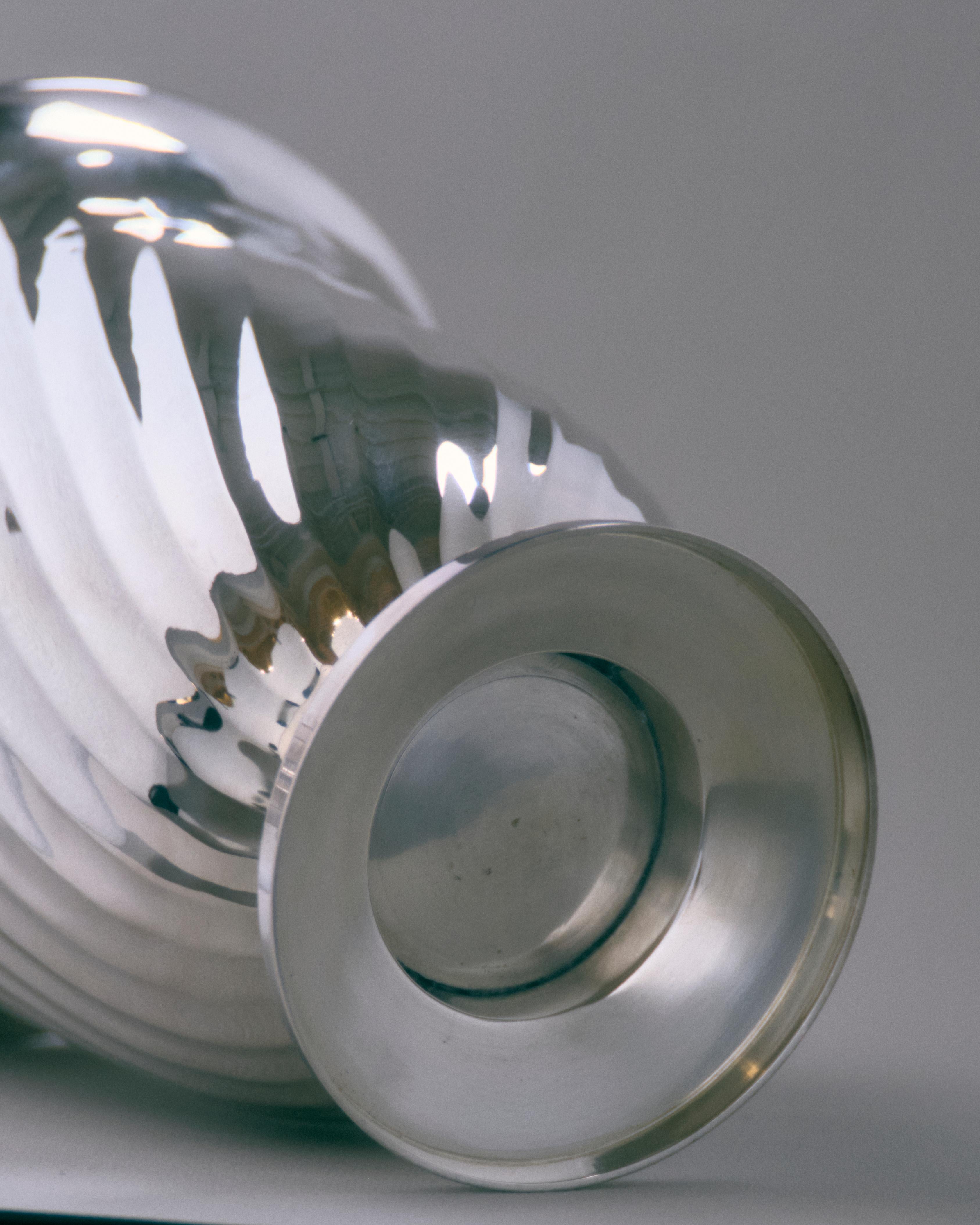 Seau à champagne en métal argenté avec un corps incurvé décoré de cannelures torsadées et reposant sur une base circulaire. Poignées latérales avec barres tournées et extrémités sphériques. Travaux européens des années 1950.