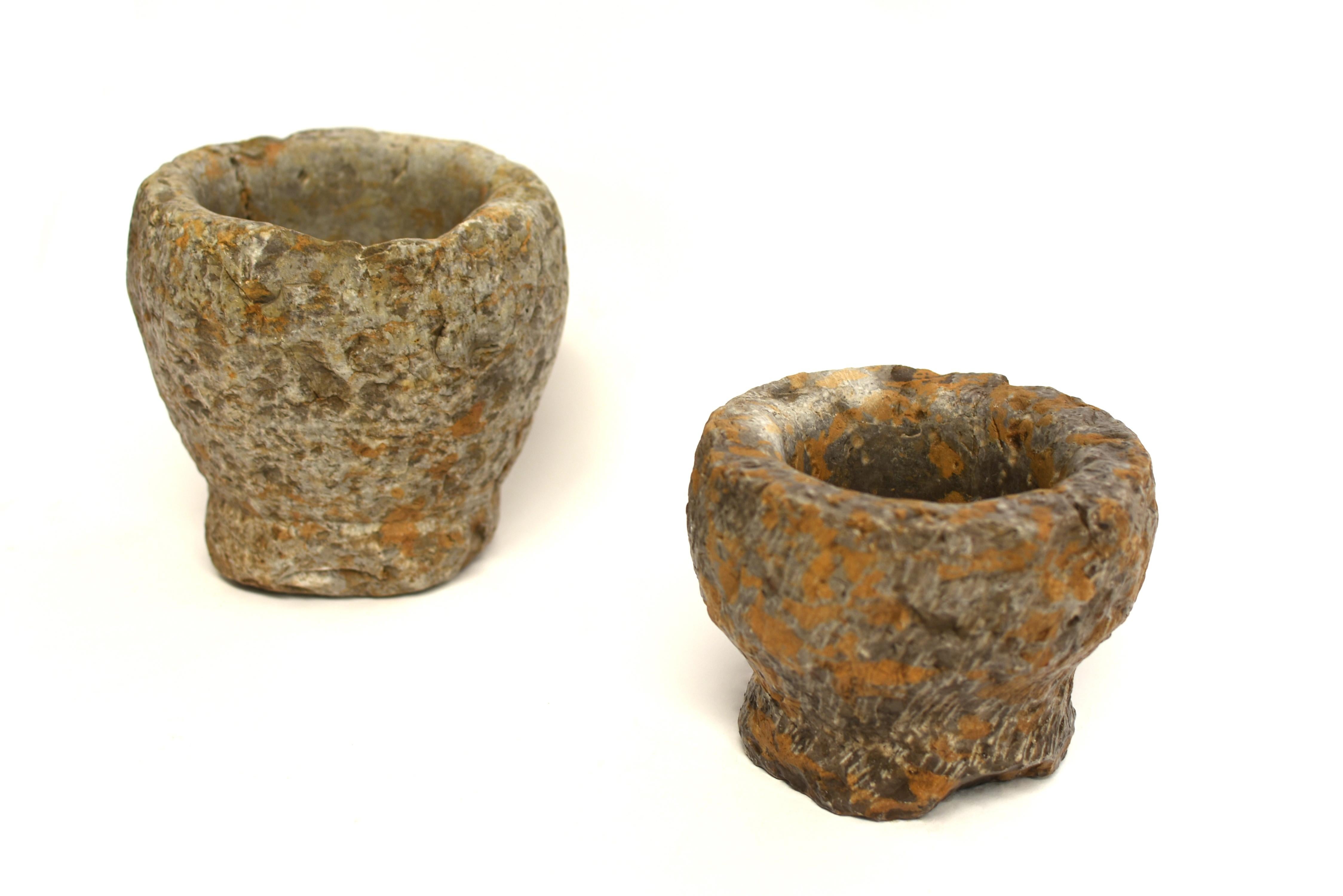 Two antique bowls of granite stone, hand cut and crafted, one in conical form on a round socle, the other hemispherical with a waisted base. The larger bowl with original hand chiseled divots, the smaller one with carved lines resembling wind blown
