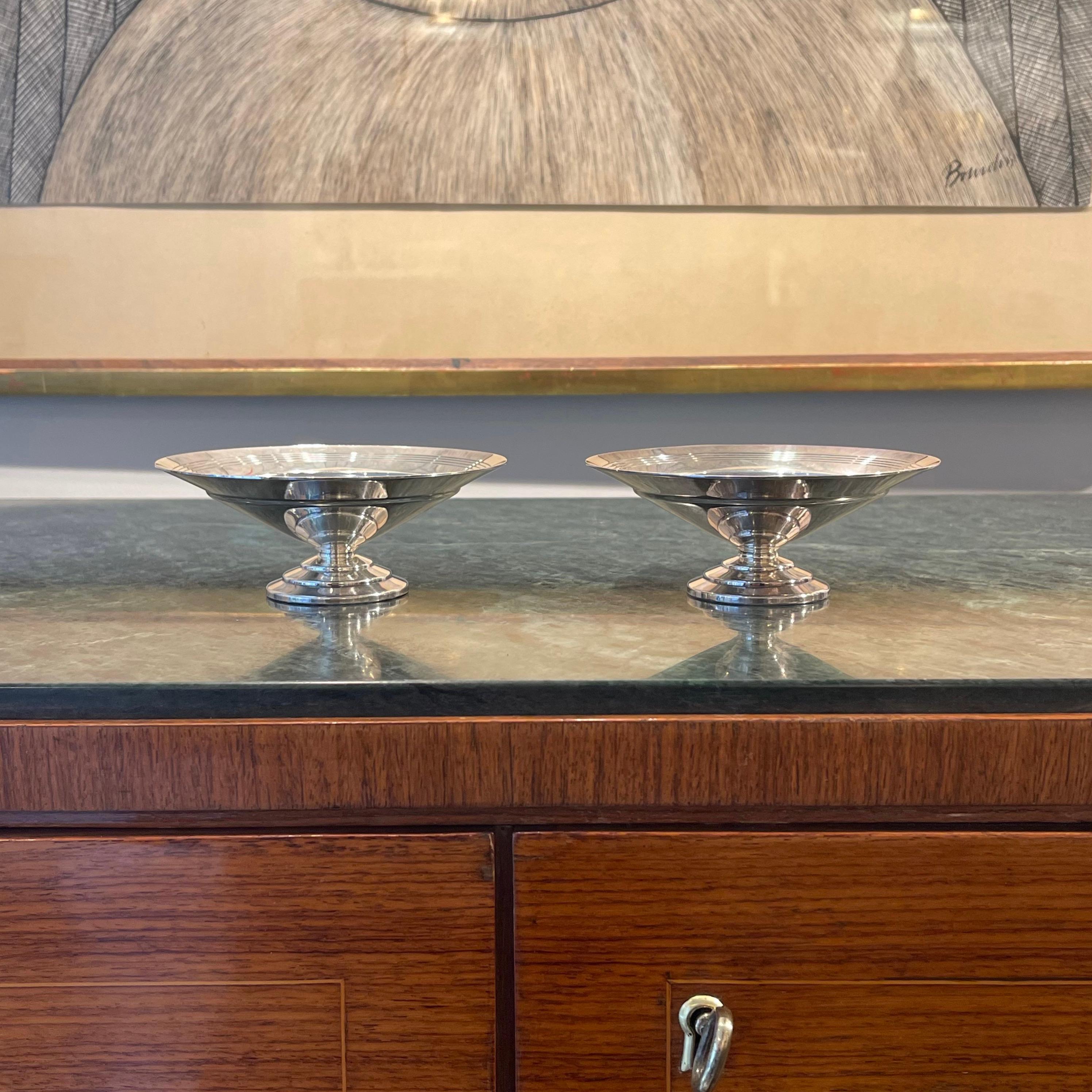Ces deux petits plats du designer britannique Keith Murray pour Mappin & Webb datent des années 1930 et illustrent le style Art déco de l'époque. Dans chaque pièce, la forme conique étagée de la base est inversée et équilibrée par le plat plus grand