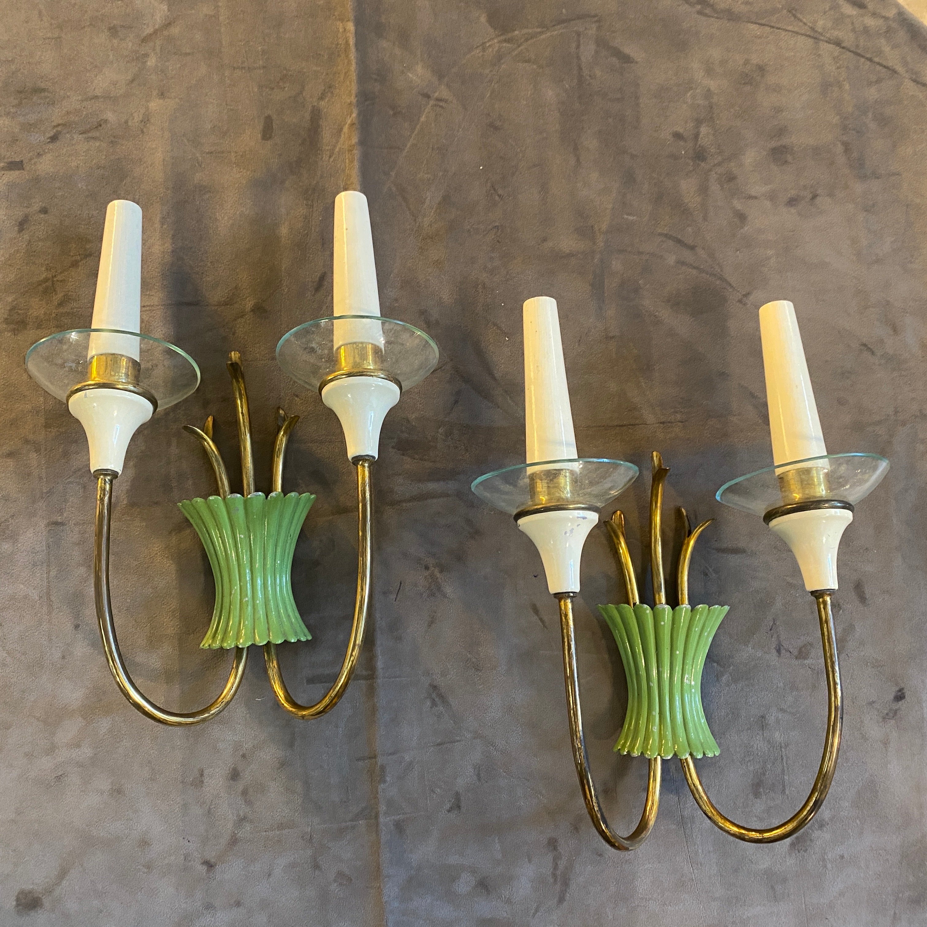 A pair of Mid-Century Modern brass, green painted metal, and glass two-light wall sconces, designed and manufactured in Italy in the fifties, are in working order and need two regular E14 bulbs for each sconce. These wall sconces are a type of