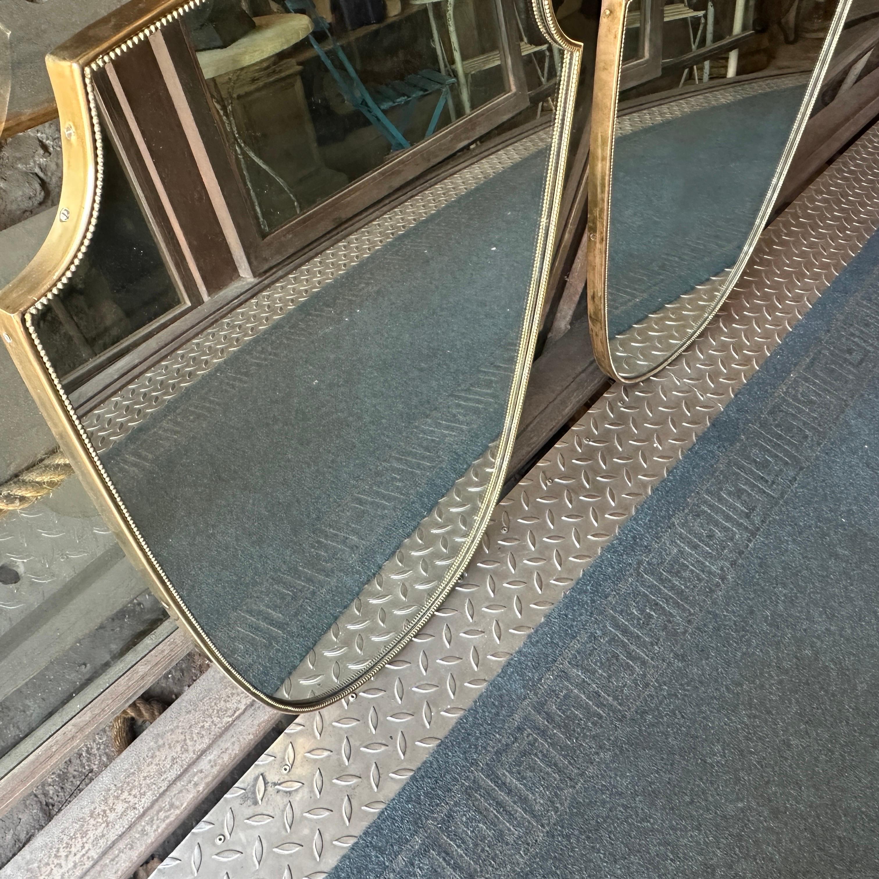 An amazing set of two solid brass wall mirrors designed and manufactured in Italy in the manner of Gio Ponti, who used this type of mirror in the most beautiful houses in Milan in the '50s. The brass is in a lovely original patina, while the glass