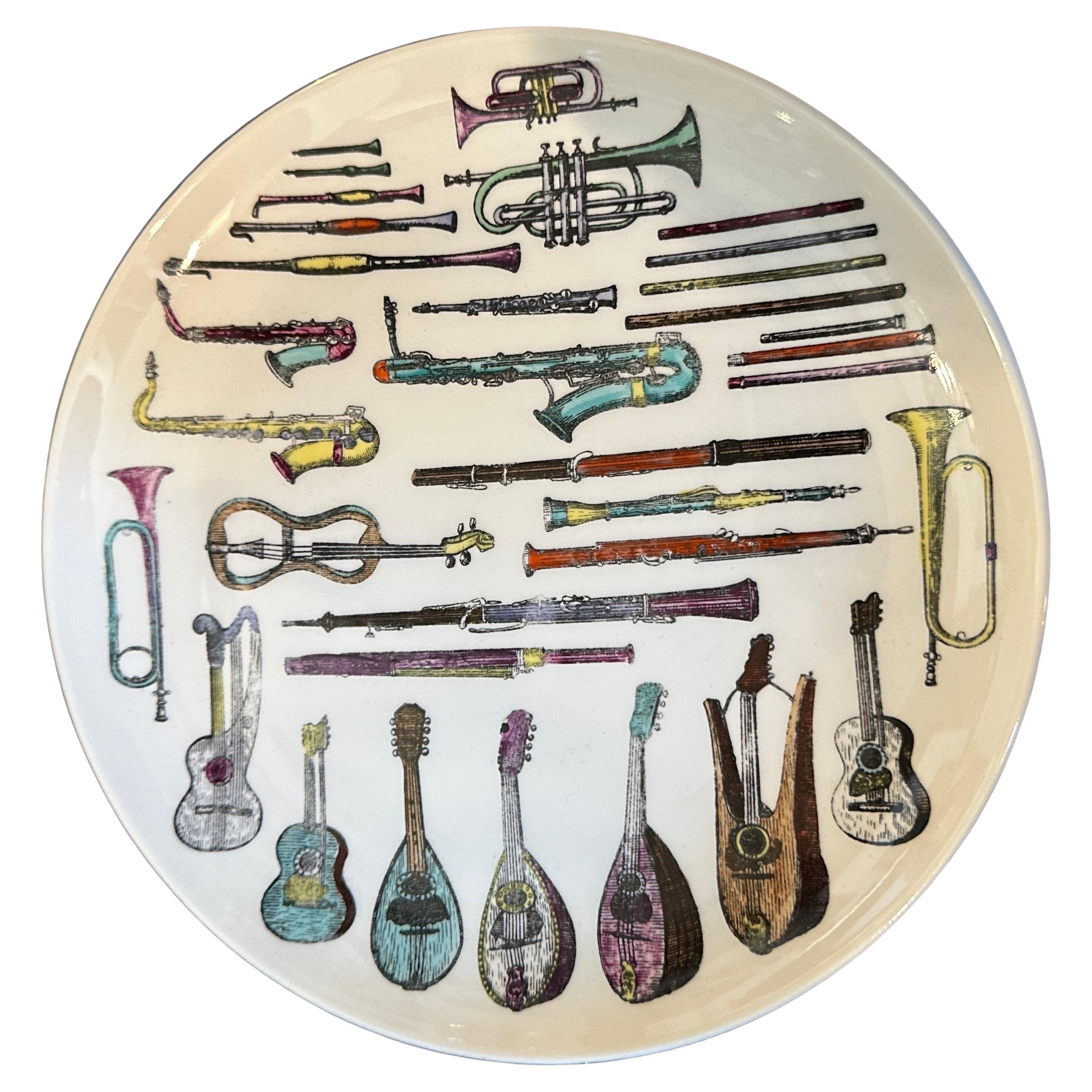 These two 1960s Mid-Century Modern decorative plates by Piero Fornasetti typically exemplify his whimsical and artistic approach to design.The plates depict intricate surreal illustrations of musical instruments, such as violins, trumpets and