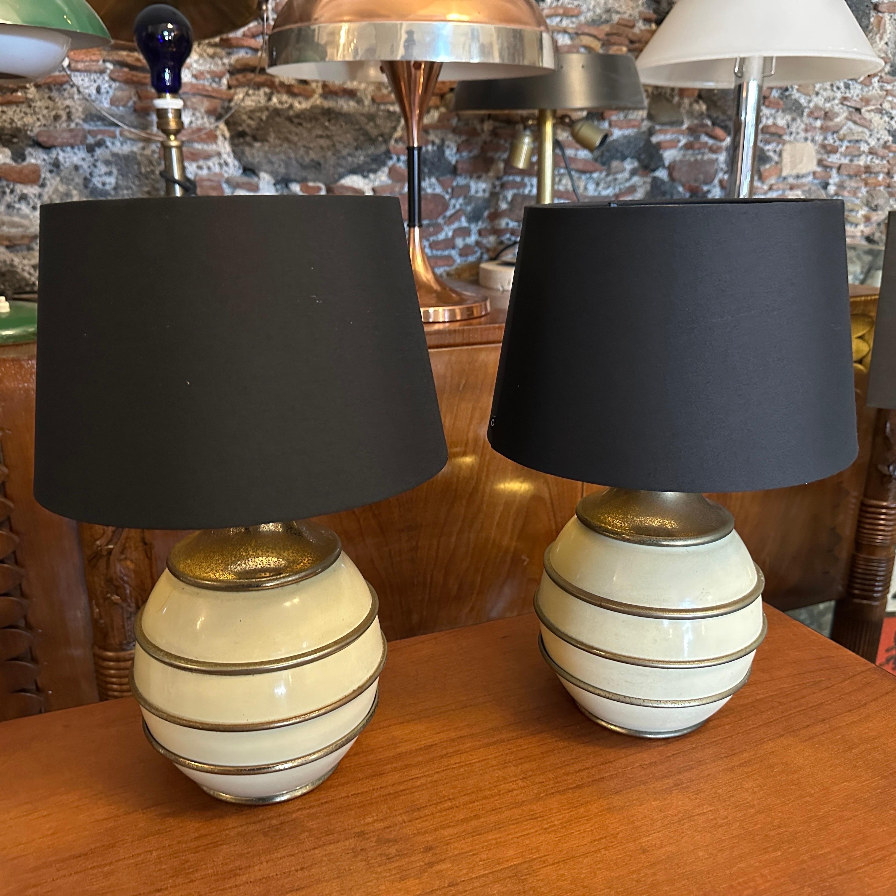 This 1970s Mid-Century Modern set of Italian table lamps, in the manner of Tommaso Barbi, exudes sophisticated elegance with its distinctive design. The base of the lamps features a layered, bulbous form crafted from ivory lacquered metal, accented