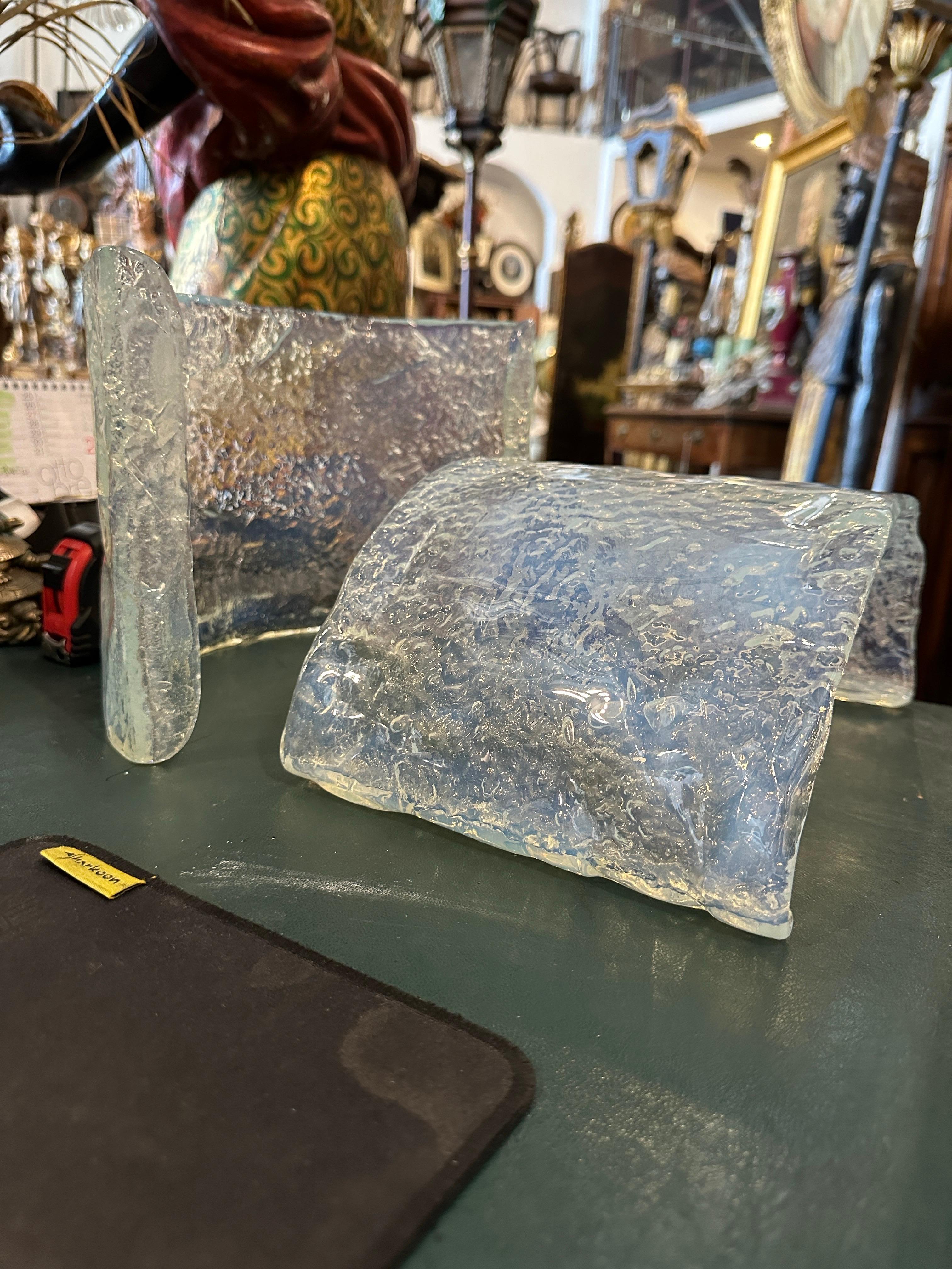 These are two 1970s Mid-Century Modern wall sconces crafted by Mazzega, a renowned Italian glassmaker known for its Murano glass designs. Each sconce features a rounded, slightly irregularly shaped shade made of opalescent Murano glass, with a