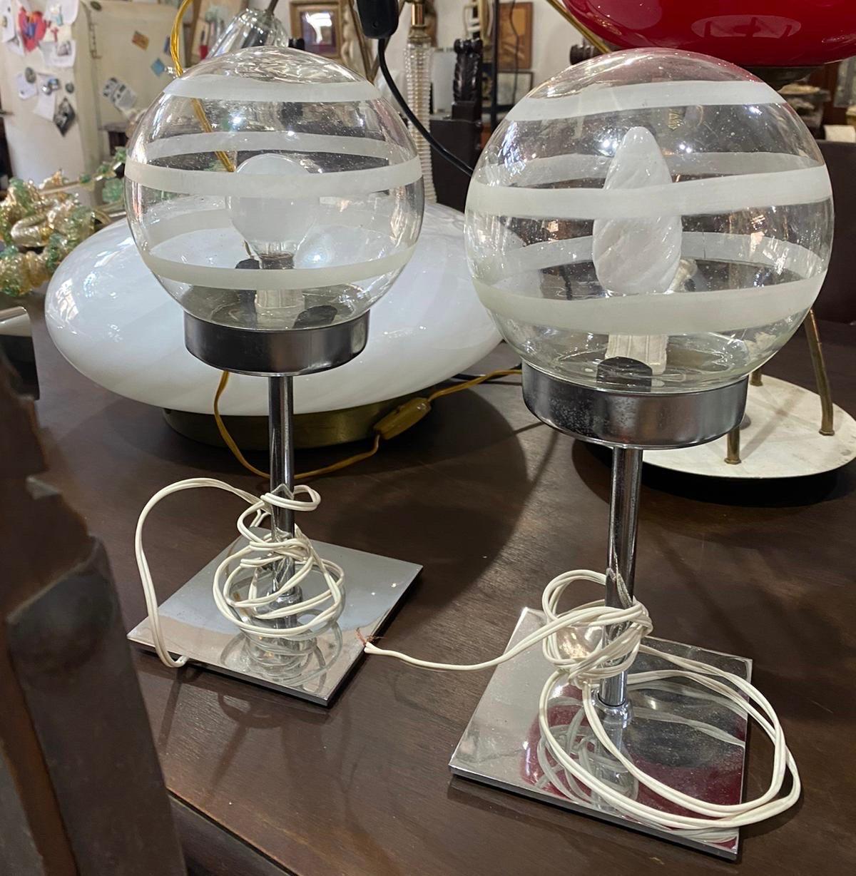 These two 1970s Space Age Murano glass bed lamps by Mazzega exhibit a stylish and futuristic design typical of the era. Each lamp features a spherical glass shade made from clear Murano glass, adorned with horizontal white stripes that wrap around