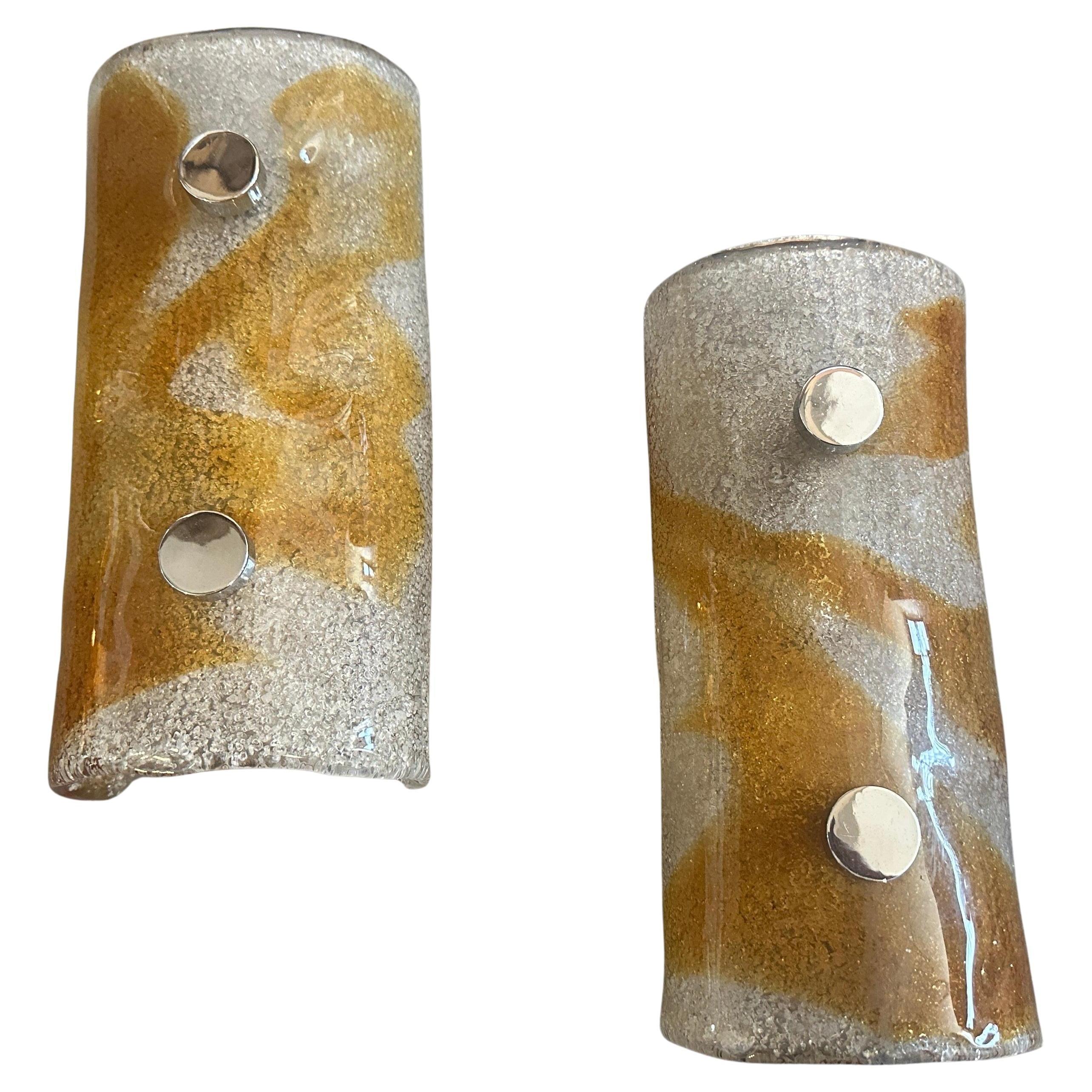 Questa splendida coppia di applique vintage italiane racchiude in sé il movimento del design A Space AGE degli anni Settanta. Ogni applique presenta un paralume semicilindrico in vetro di Murano spesso e curvo. Il vetro stesso è una miscela