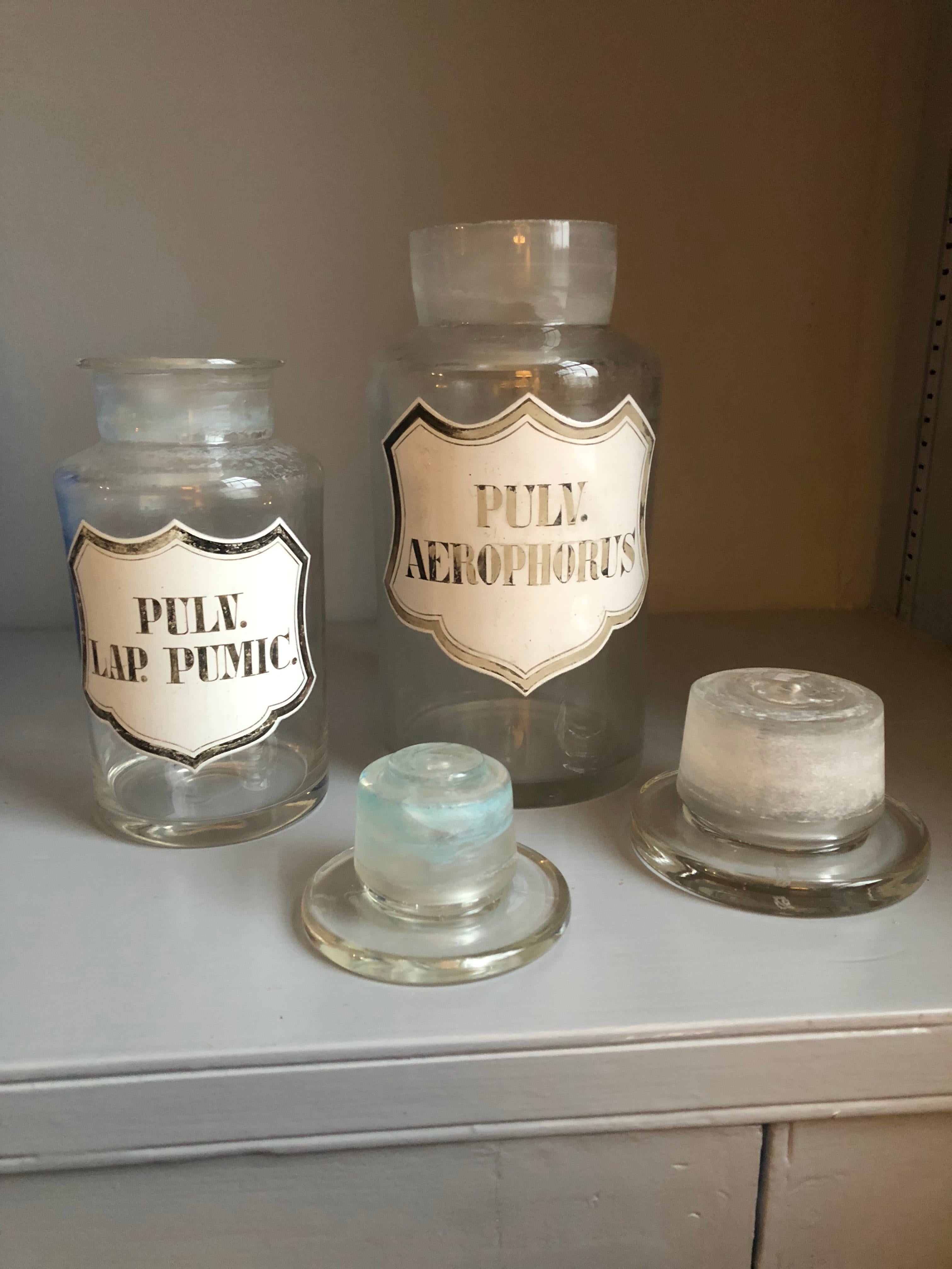 Two 19th century hand blown apothecary jars with enamel labels with silver leaf lettering each retaining its original glass stopper. The larger of the two measures 4” diameter x 9” height, the smaller, 3” diameter x 7” high.