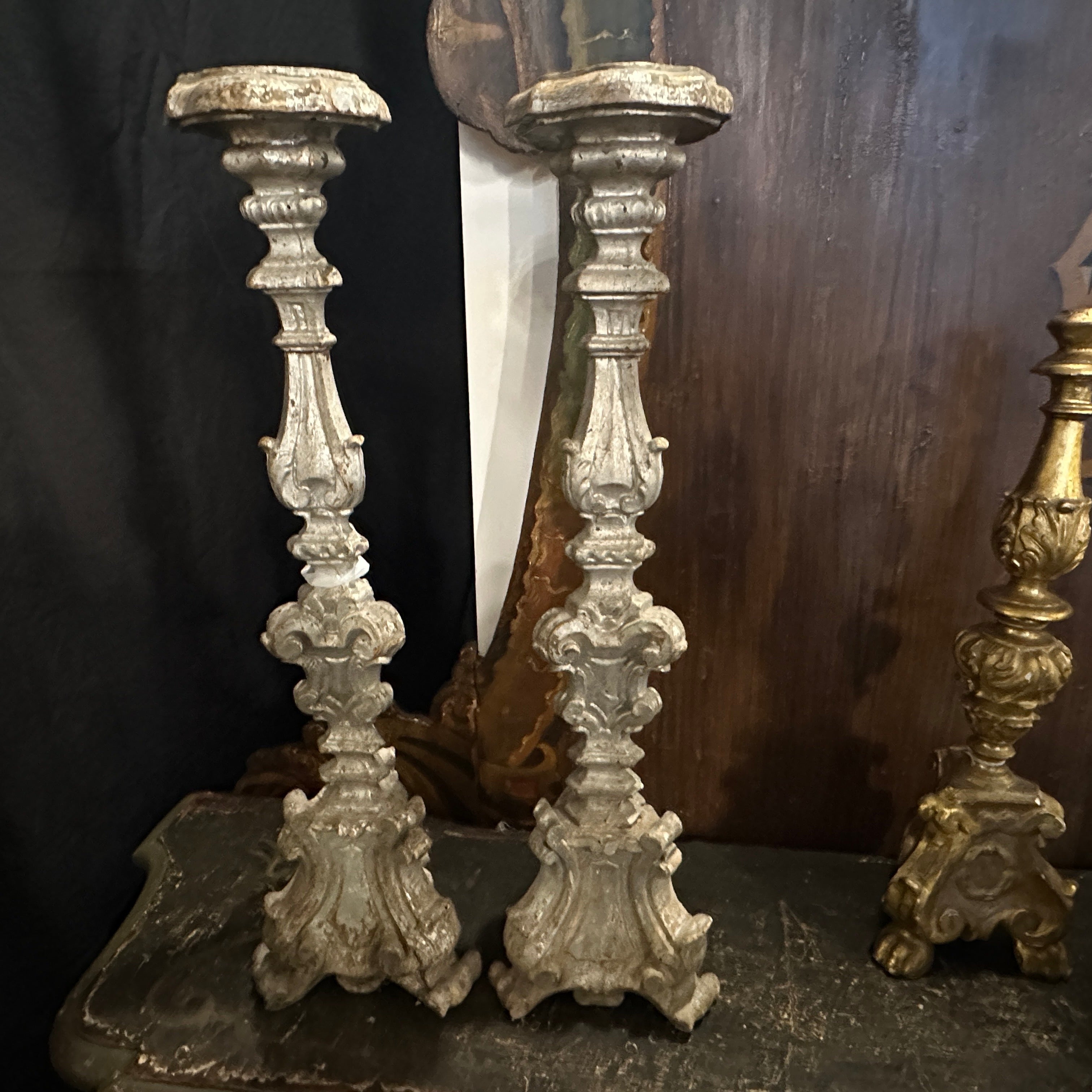 Une rare paire de torchères baroques siciliennes du XIXe siècle, magistralement sculptées à la main dans du bois massif et finies avec une surface argentée usée par le temps. Ces chandeliers statuaires illustrent la grandeur théâtrale de