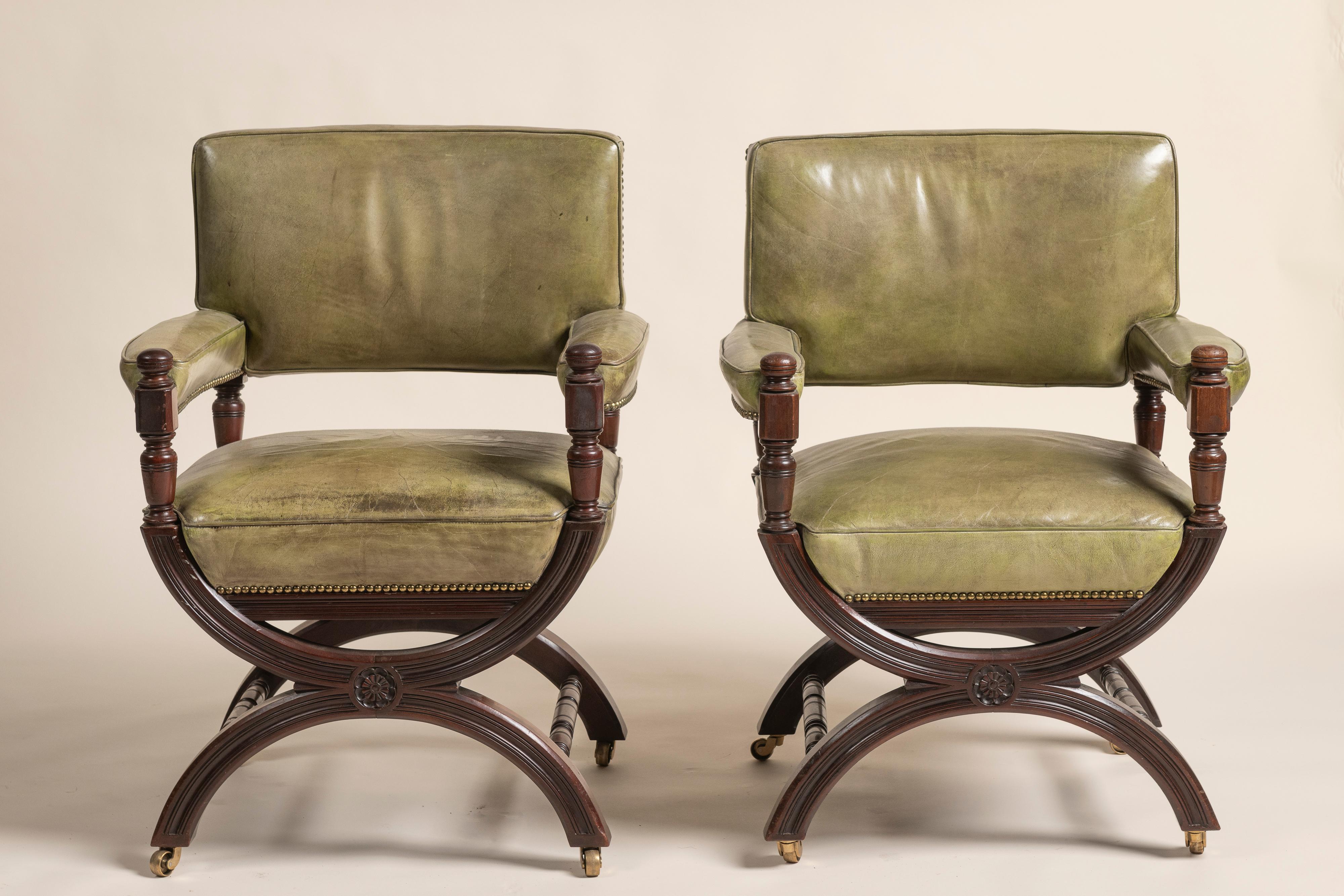 Cette fantastique paire de fauteuils anglais du XIXe siècle, avec une variante du design en X, est fabriquée en acajou et recouverte d'un cuir patiné vert olive. Les pieds sculptés, les clous décoratifs en laiton posés à la main et les accoudoirs