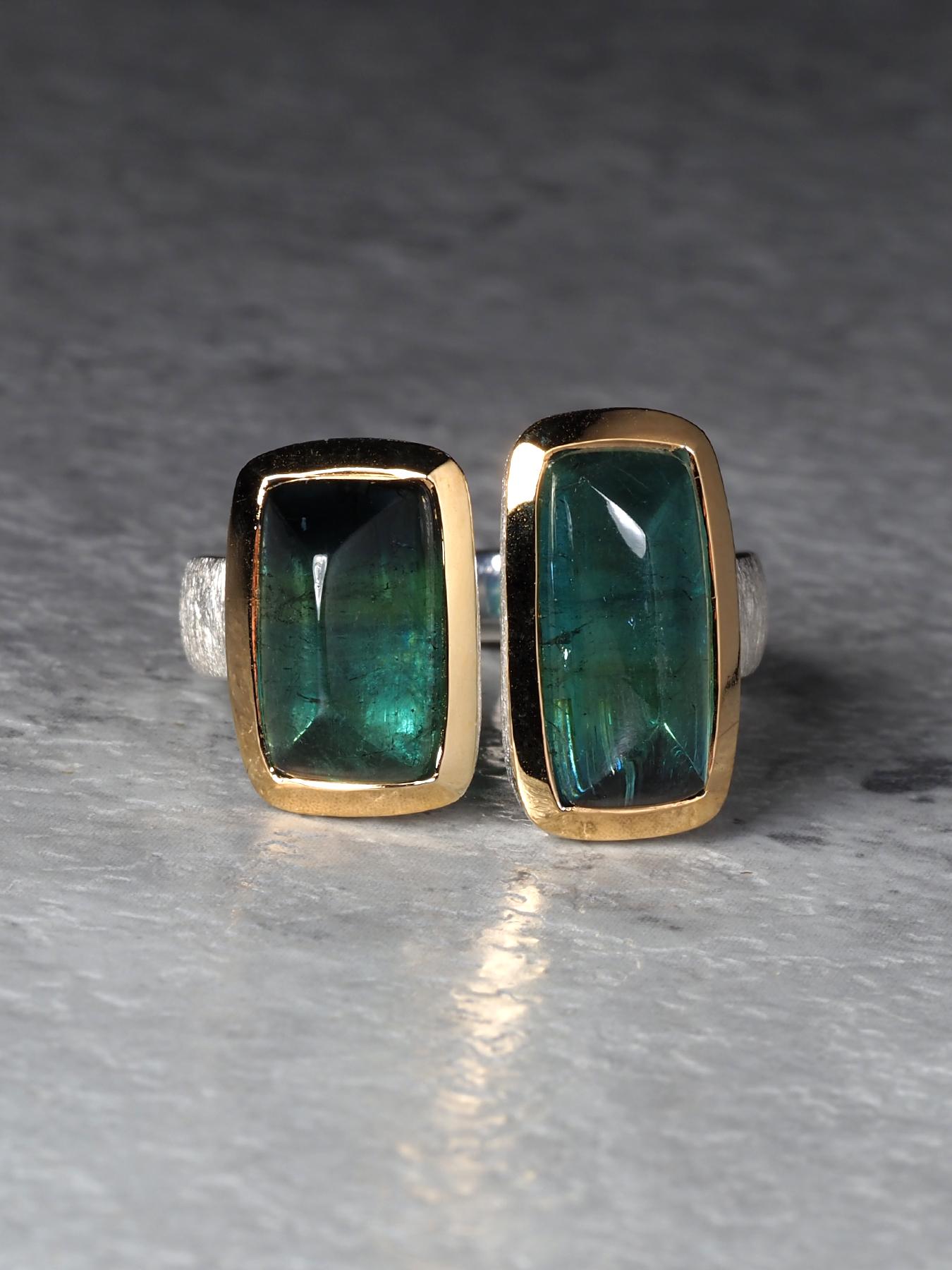 Un anello contemporaneo di grande effetto che mette in mostra due tormaline verdi naturali del Brasile per un peso totale di 7 carati. Ogni gemma è tagliata nel raro stile cabochon a forma di pan di zucchero e misura 6 x 10 mm e 6 x 12 mm. Le loro