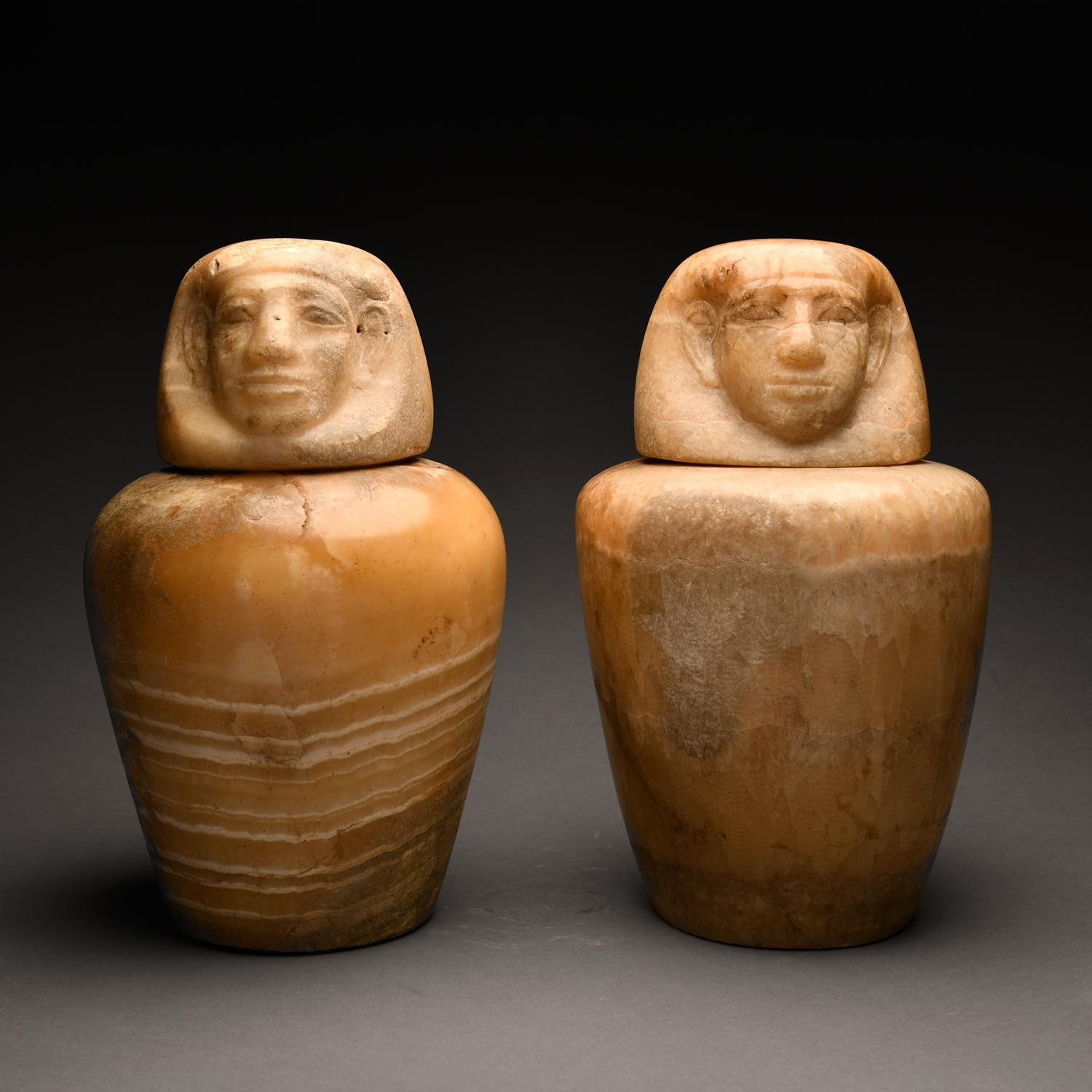 This set of two canopic jars represents unequivocal masterpieces of the type.  Carved out of a beautifully rich white veined caramel alabaster, both jars are deftly executed and of robust, elegant proportion.  Each with rounded shoulders tapering to