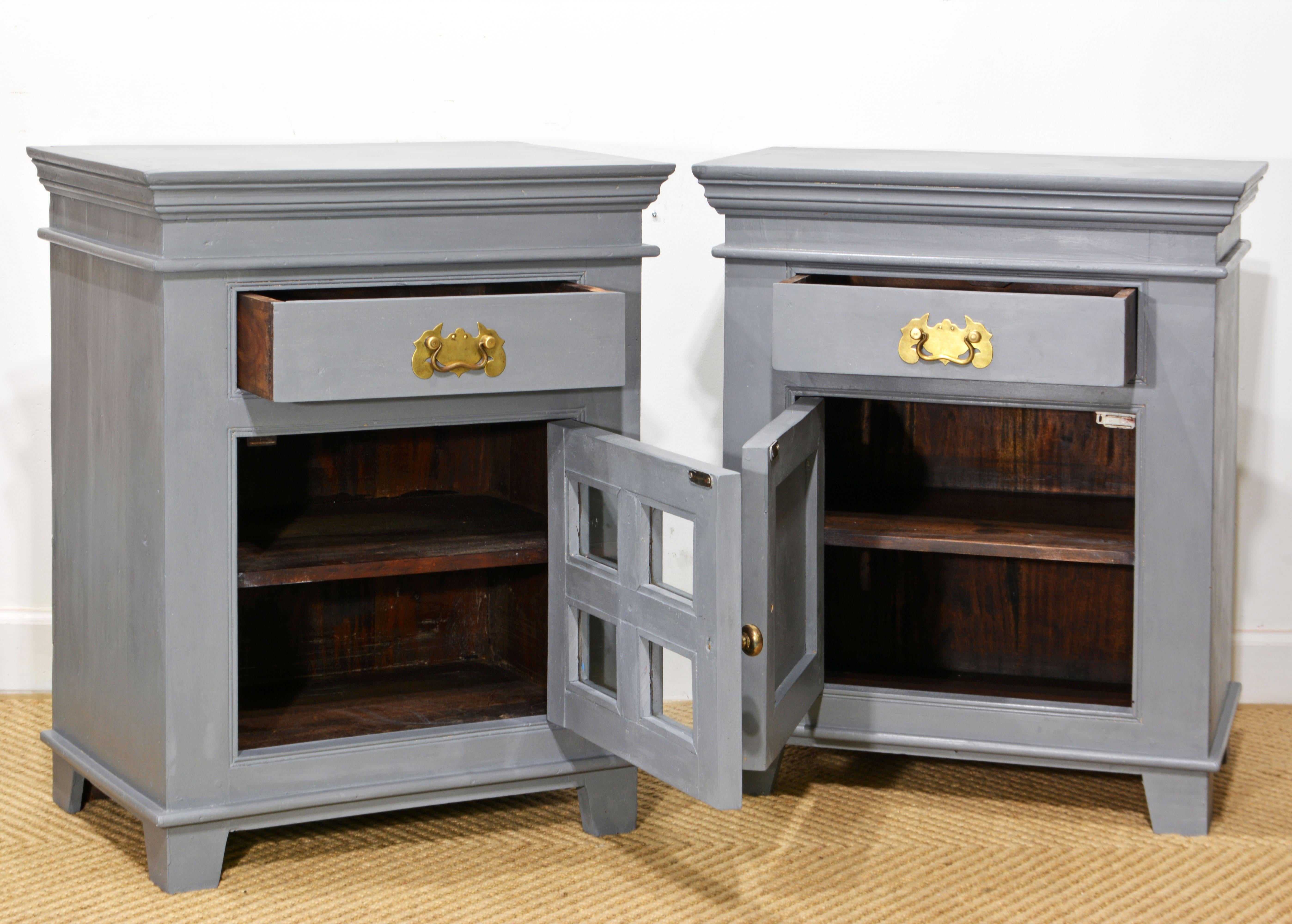 This almost pair of Anglo-Indian bedside cabinets or nightstands are made of solid hardwood which has later been painted in a 'officer's grey' color and wax buffed creating a subtle aged and layered look. One of the cabinets has had glass panels