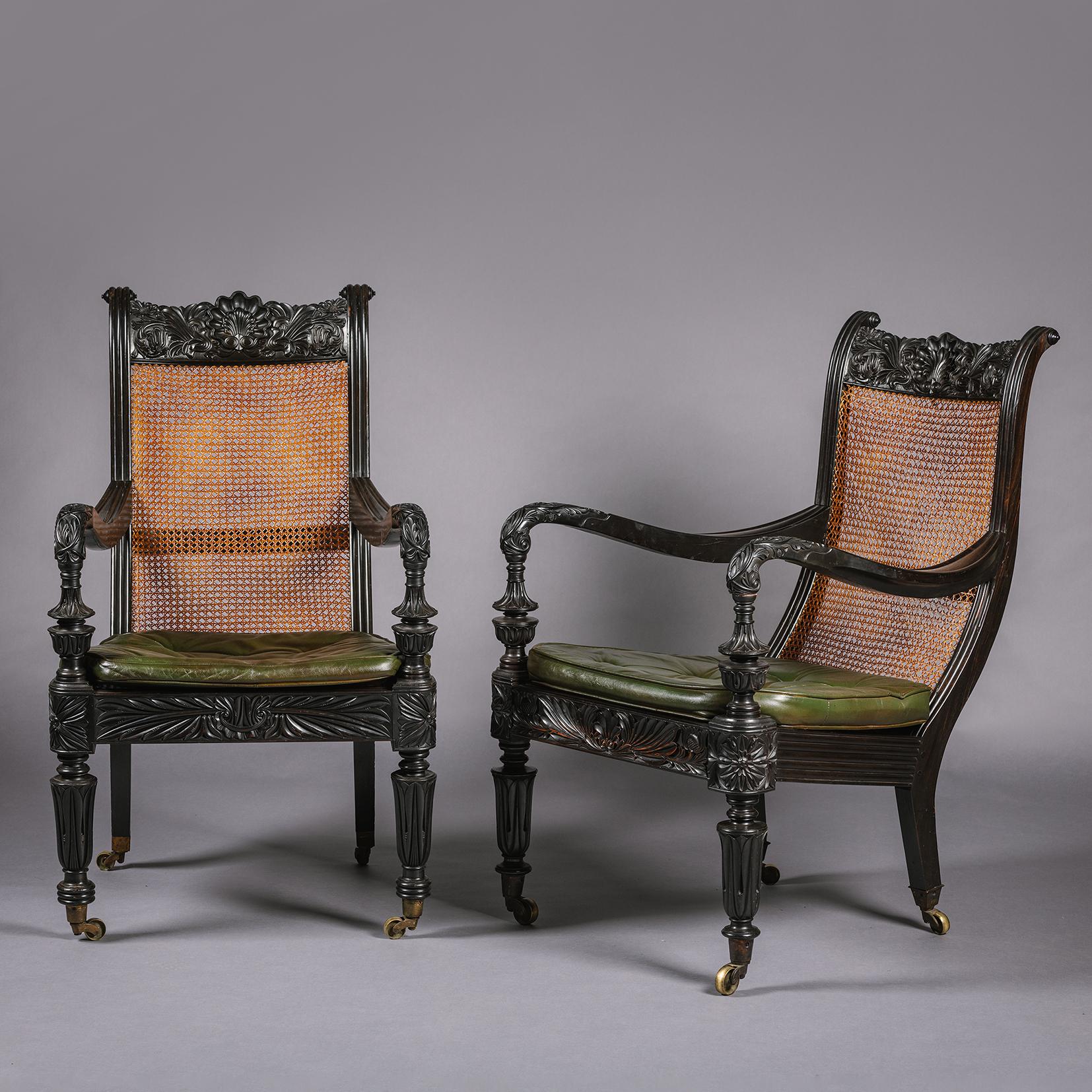 Two Anglo-Indian Carved Ebony Easy Armchairs. 

Each with tablet toprail elaborately carved with stylised flower-head and scrolling foliage around a central scallop shell. The channelled side rails running to swept arms with leaf carved terminals